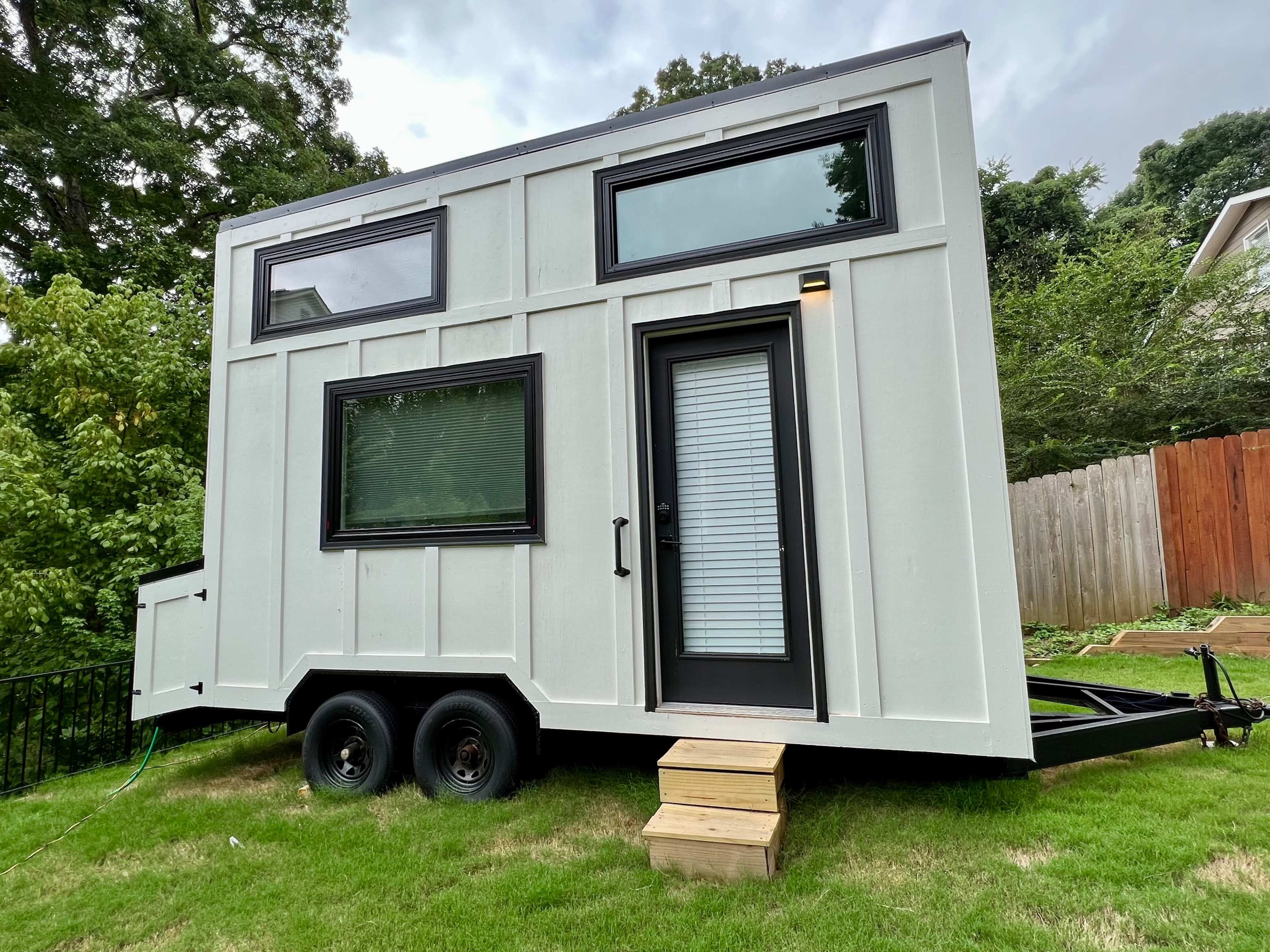 A modern tiny house on wheels, featuring large windows and a front door, situated on a grassy area.