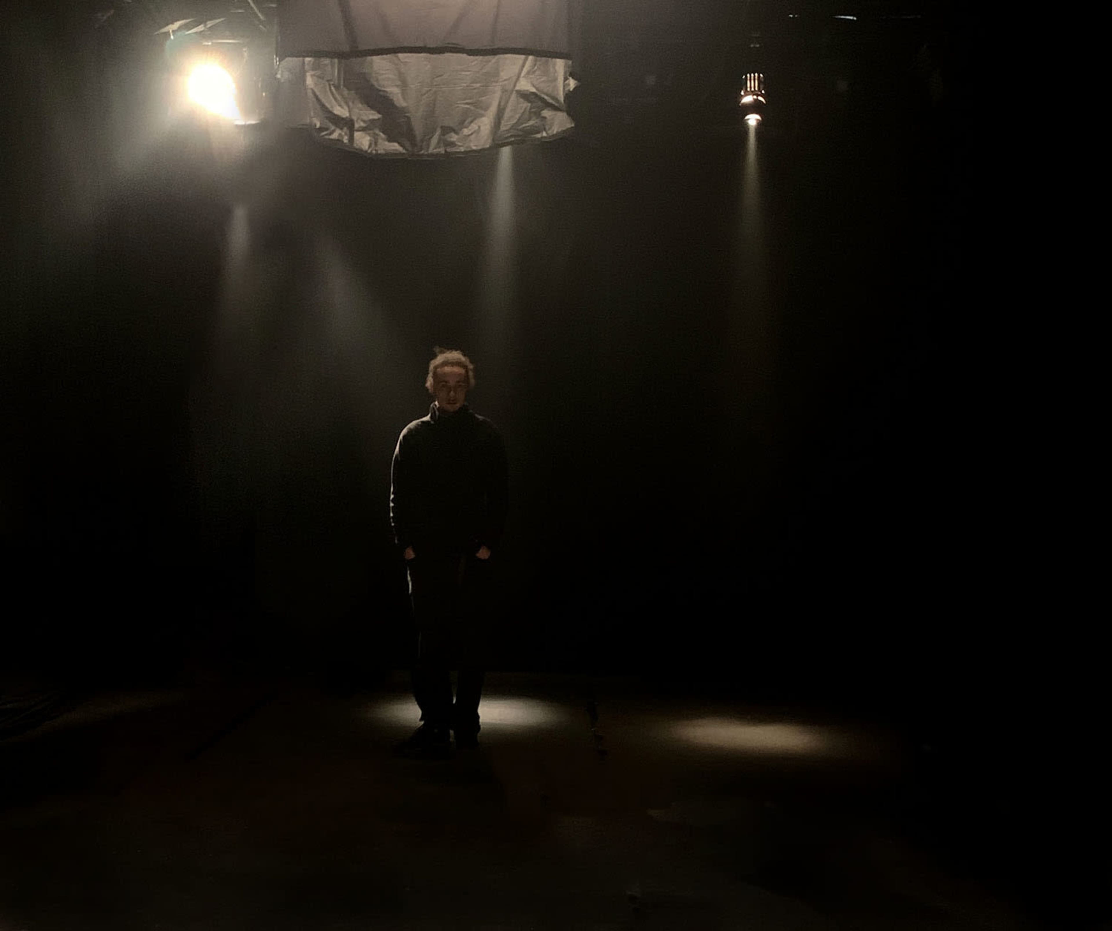 A person stands in a dimly lit space under focused spotlights.