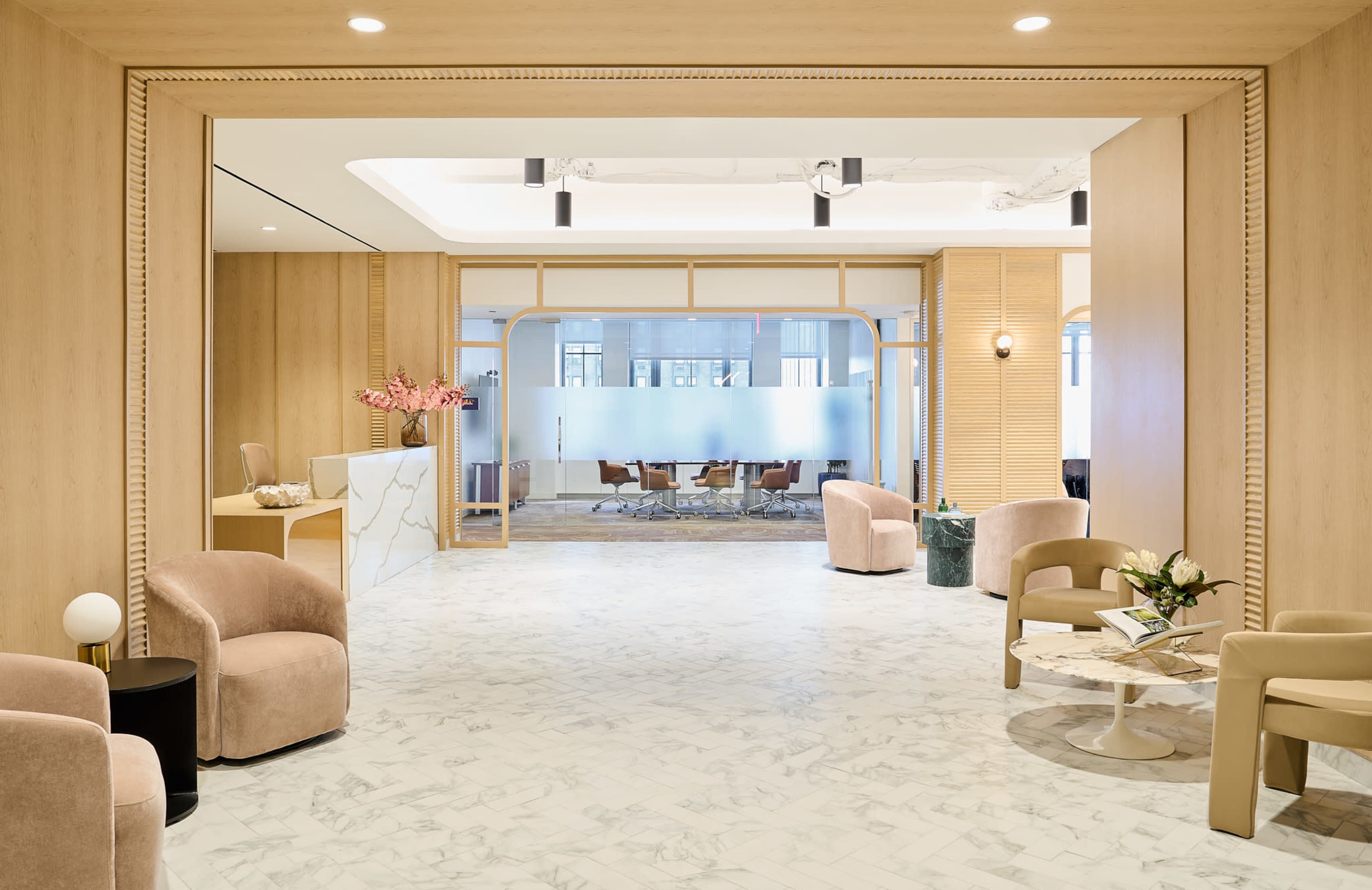 A spacious, modern lobby features marble flooring, wooden accents, and seating arrangements with plush chairs and a small coffee table.
