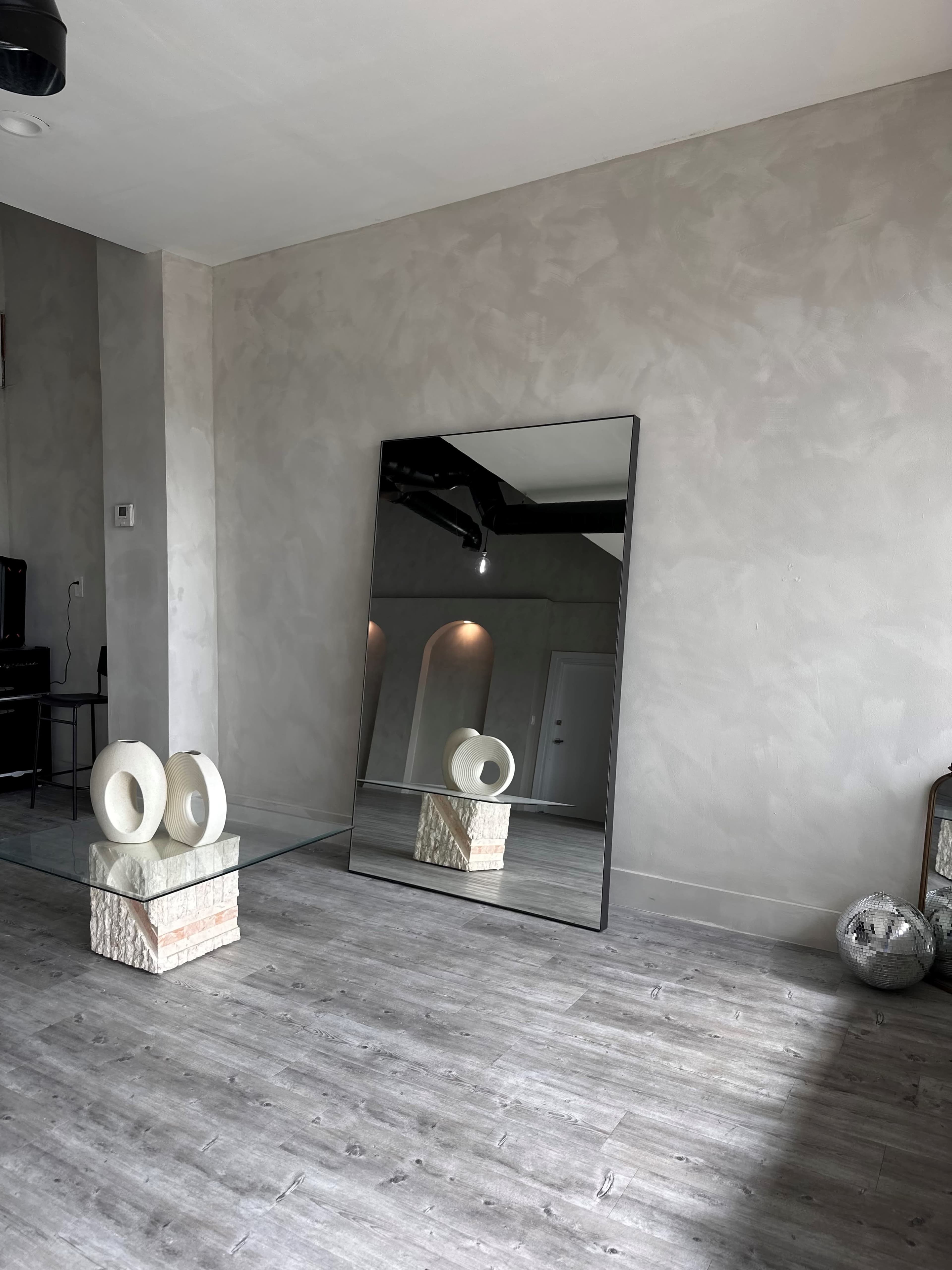 A spacious room featuring a large mirror, a decorative stone pedestal with circular objects, and a minimalist design.