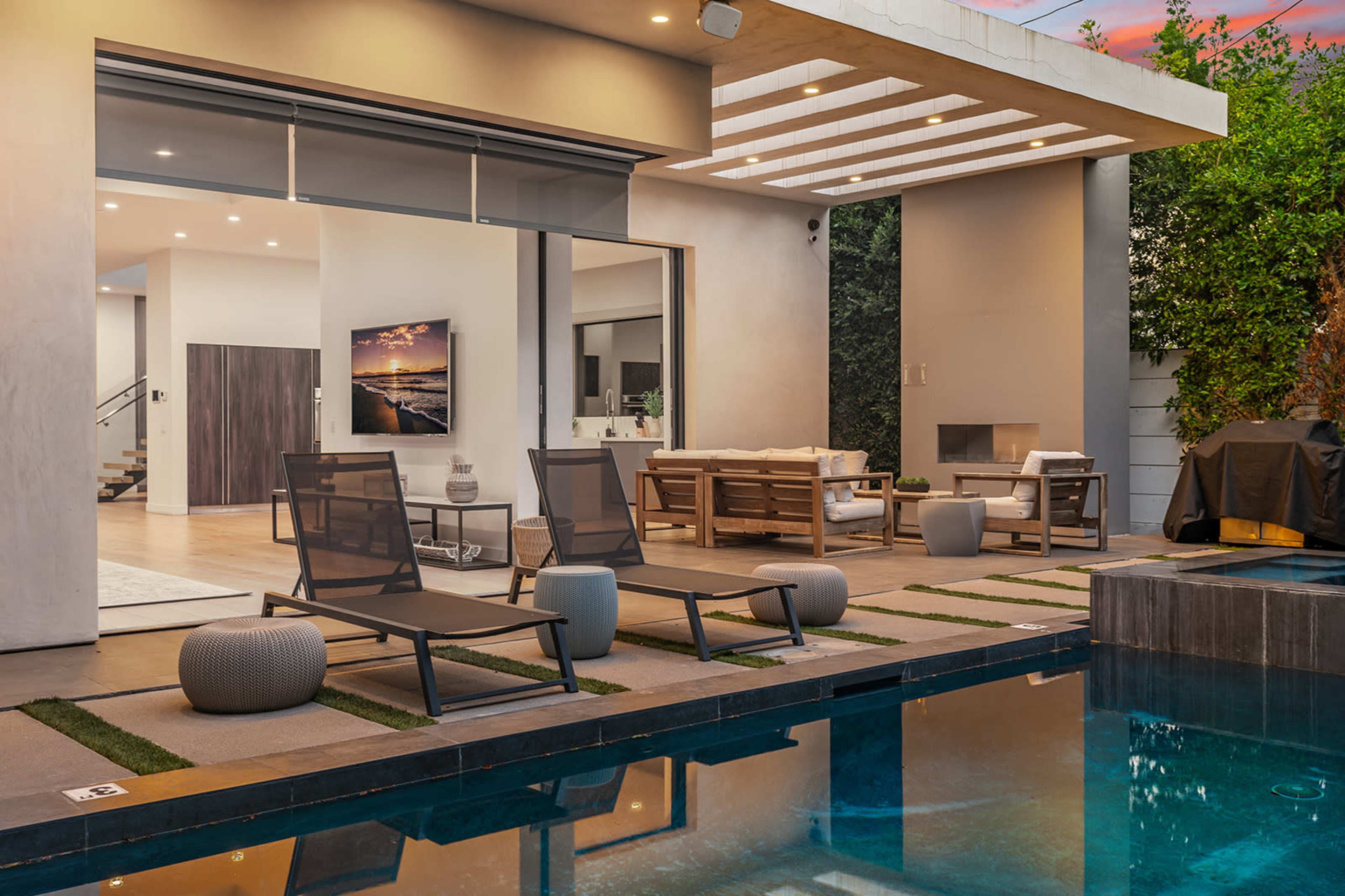 A modern outdoor space features lounge chairs by a reflective pool, adjacent to a stylish living area with large windows and a cozy seating arrangement.