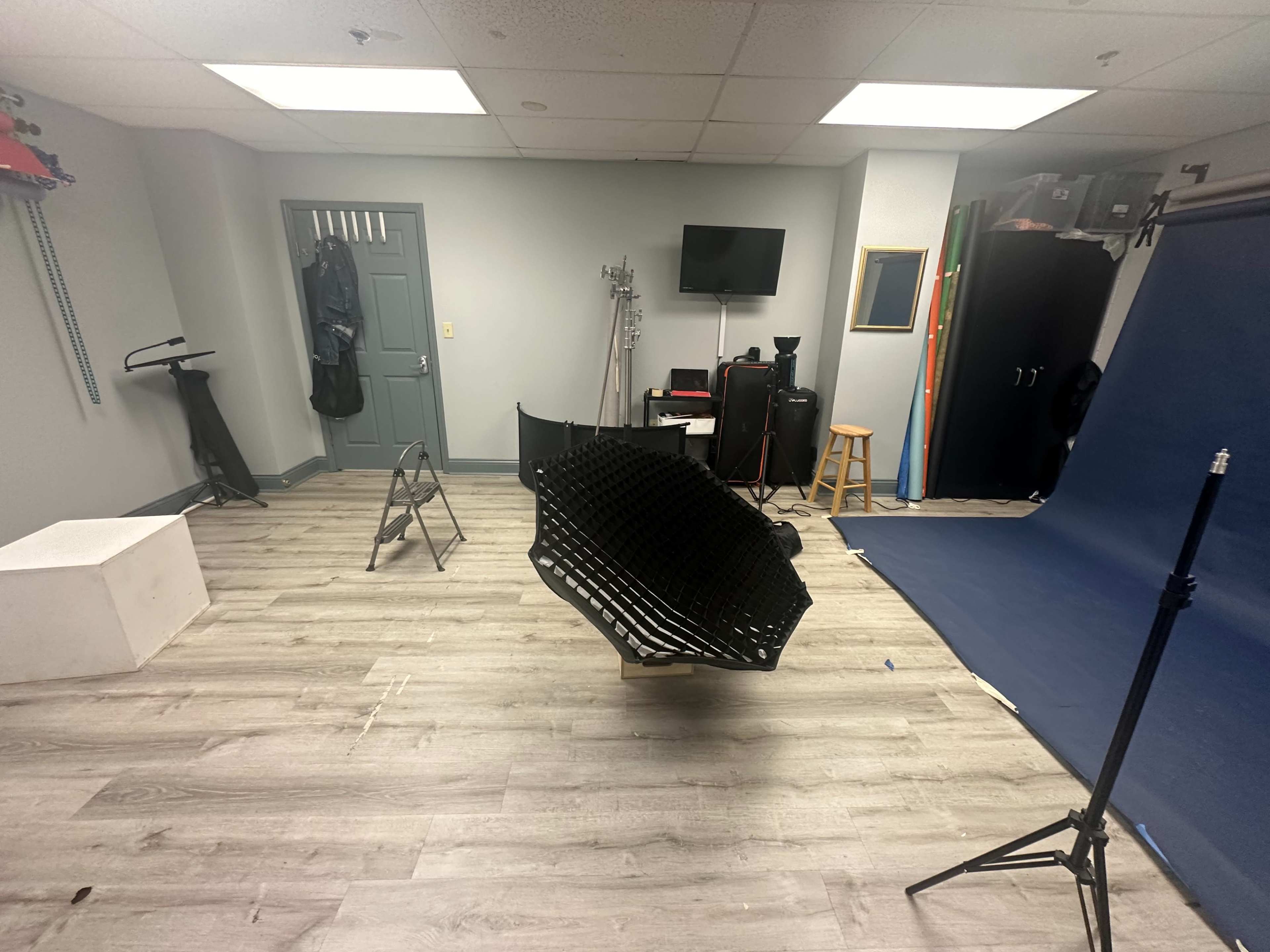 A photography studio with a blue backdrop, a white platform, a chair, and various equipment arranged around the room.