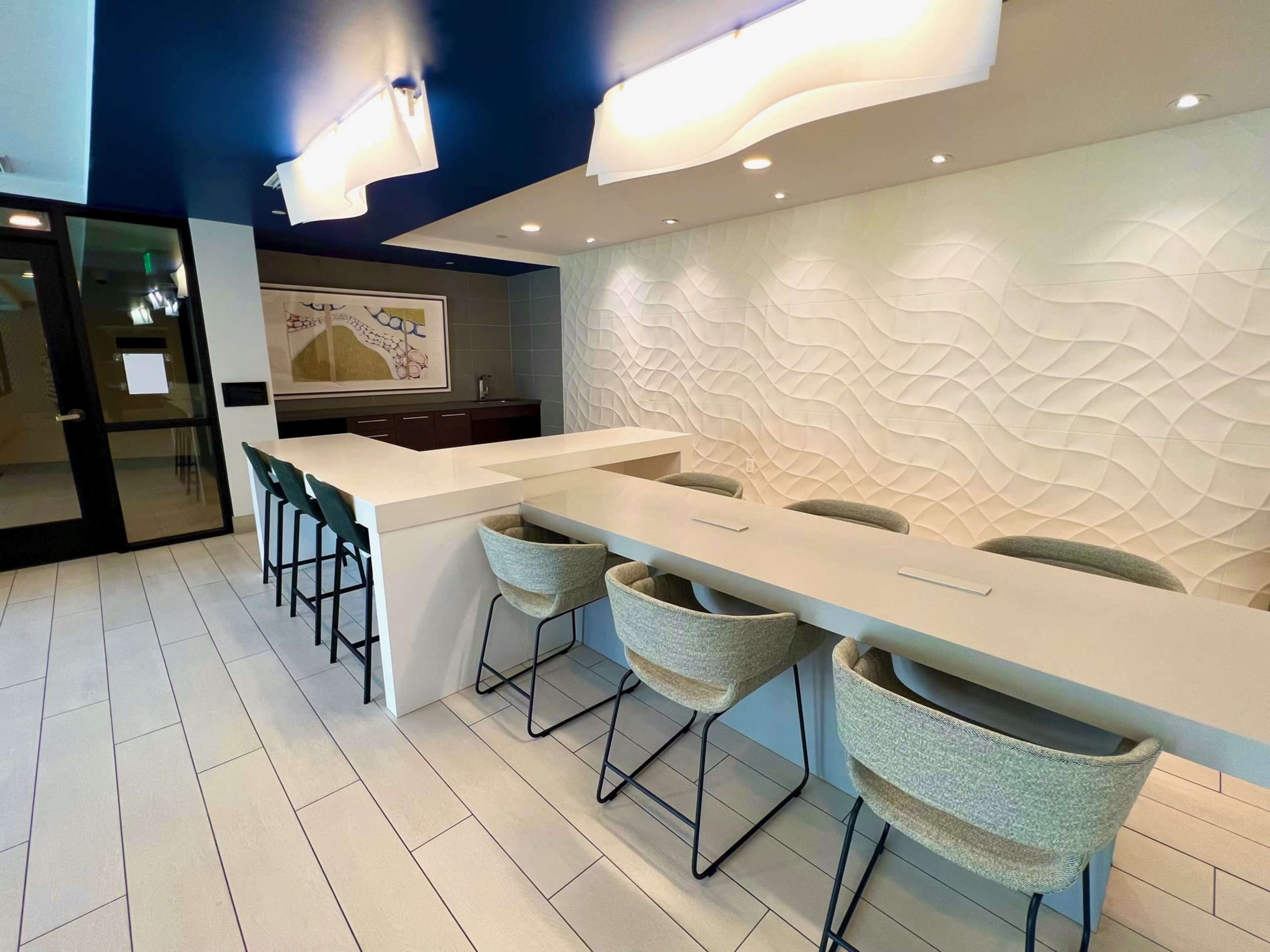 A modern kitchen or bar area with a long, white countertop and high-backed chairs against a textured wall.