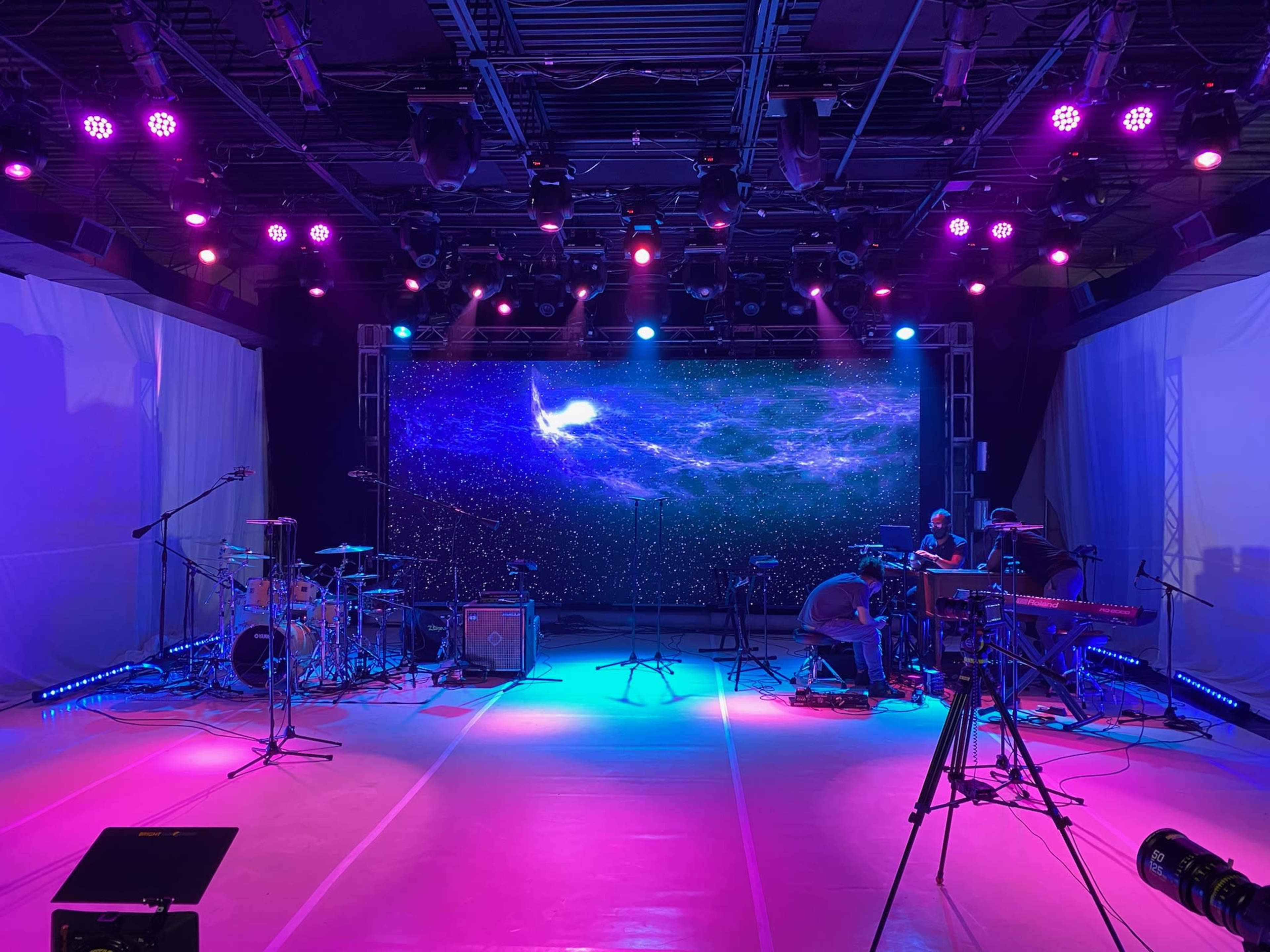 A stage set up for a performance, featuring musical instruments, microphones, and a large backdrop with a cosmic-themed projection.
