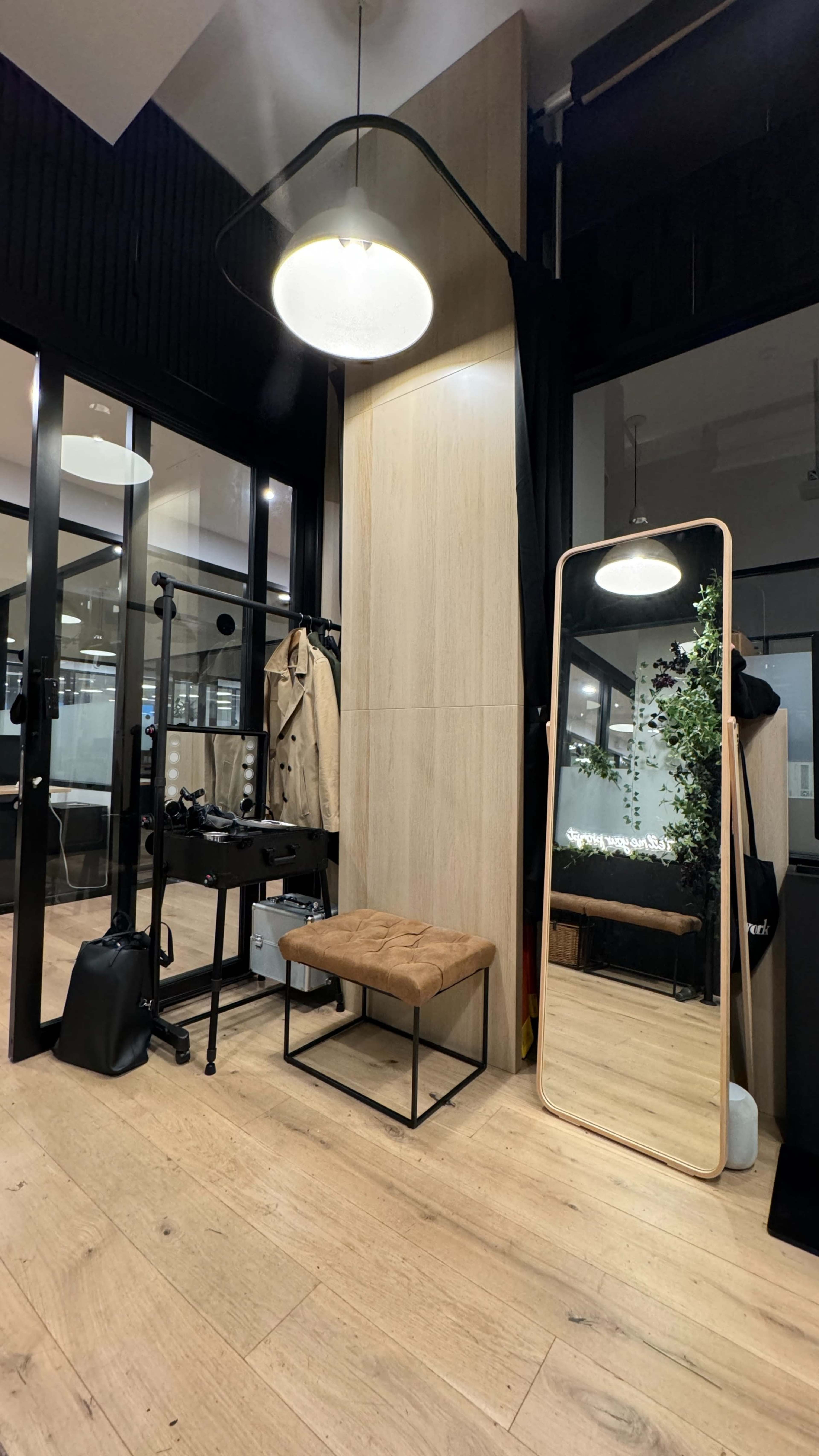 A modern dressing area featuring a large mirror, a bench, clothing racks, and a light fixture in a stylish interior space.