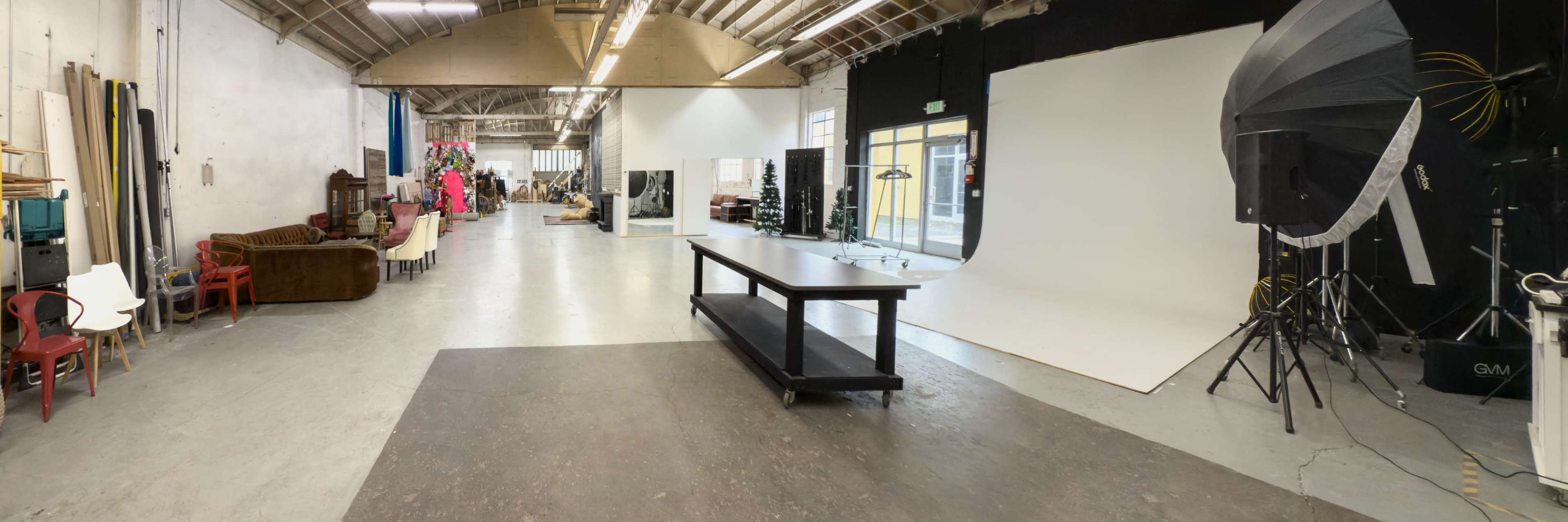 The image shows a spacious photography studio with equipment, seating areas, and a large white backdrop.