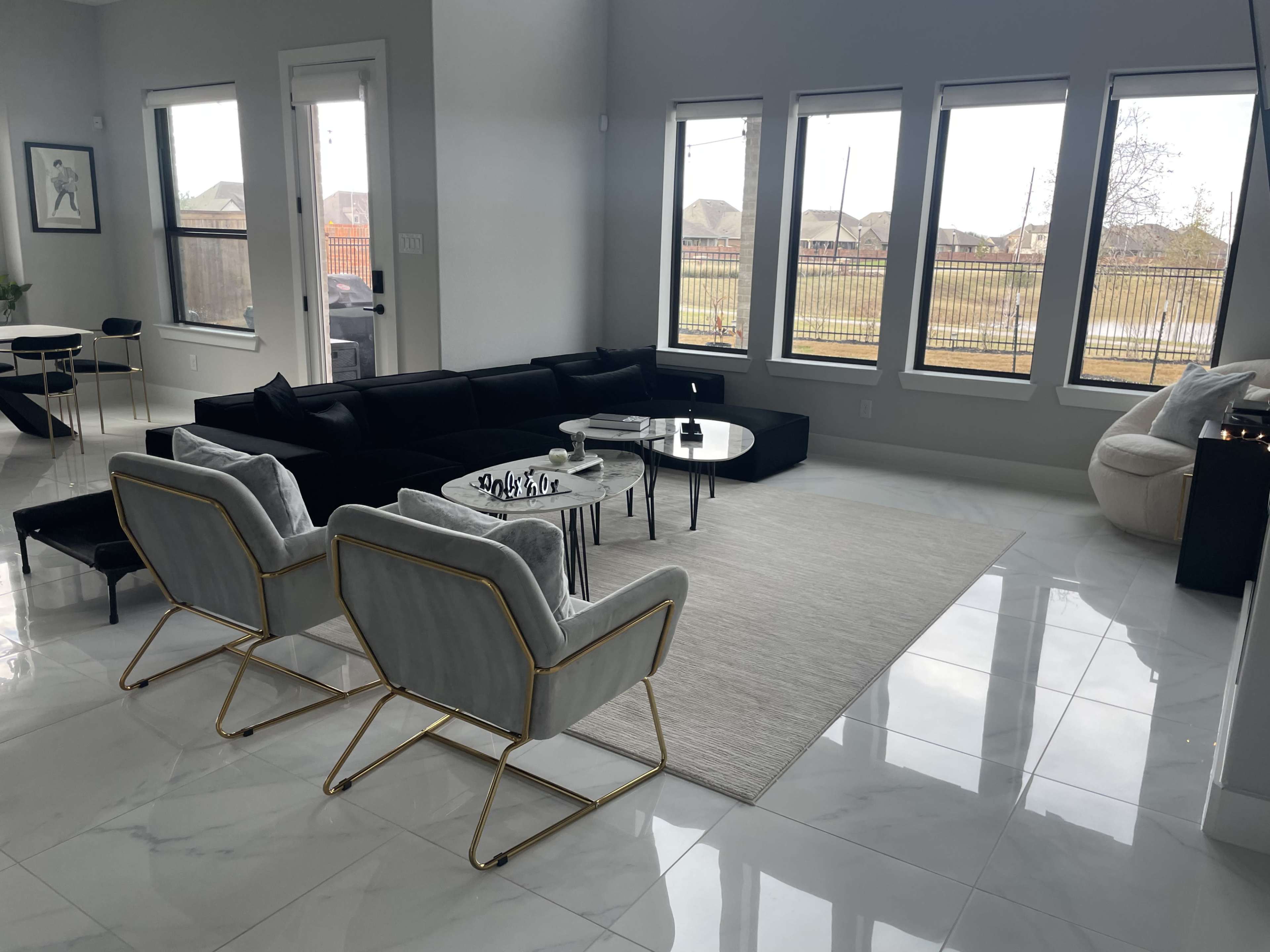 A modern living room with a sectional sofa, two armchairs, a coffee table, and large windows overlooking a fenced outdoor area.