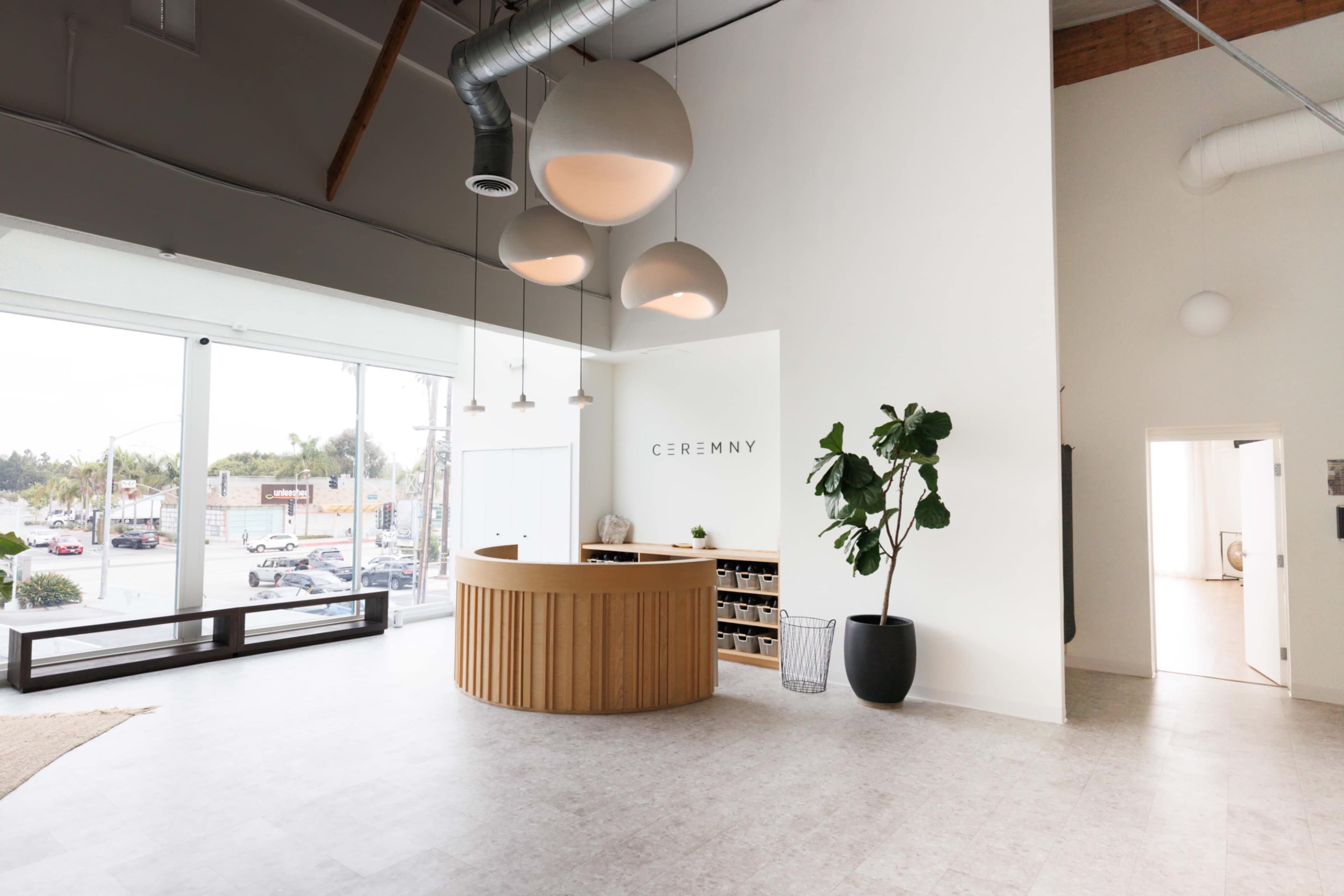 A modern reception area features a circular wooden front desk, large windows with street views, and minimalist decor.