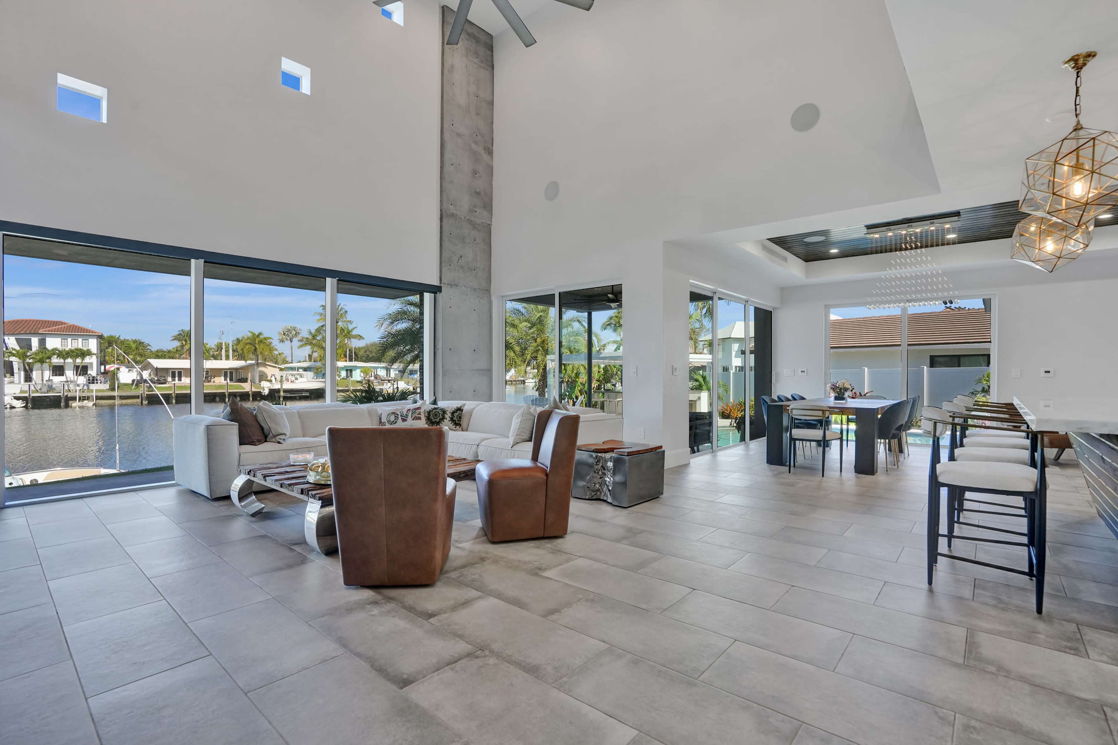 The image features a modern living area with large windows overlooking a marina, furnished with a white sofa, wooden coffee table, and a dining area near a sleek kitchen.