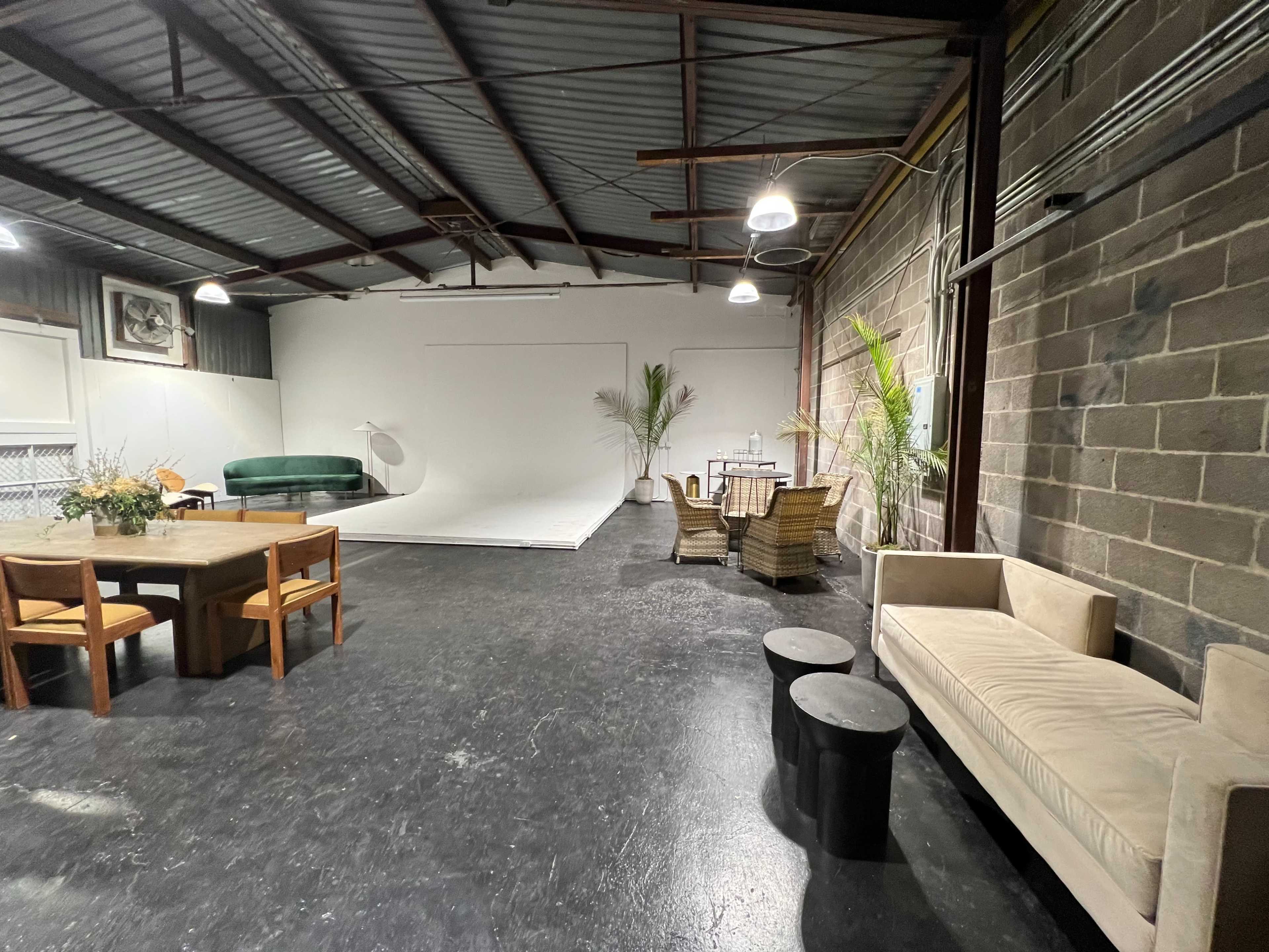 An industrial-style studio space with a seating area, a dining table, and a large white backdrop.