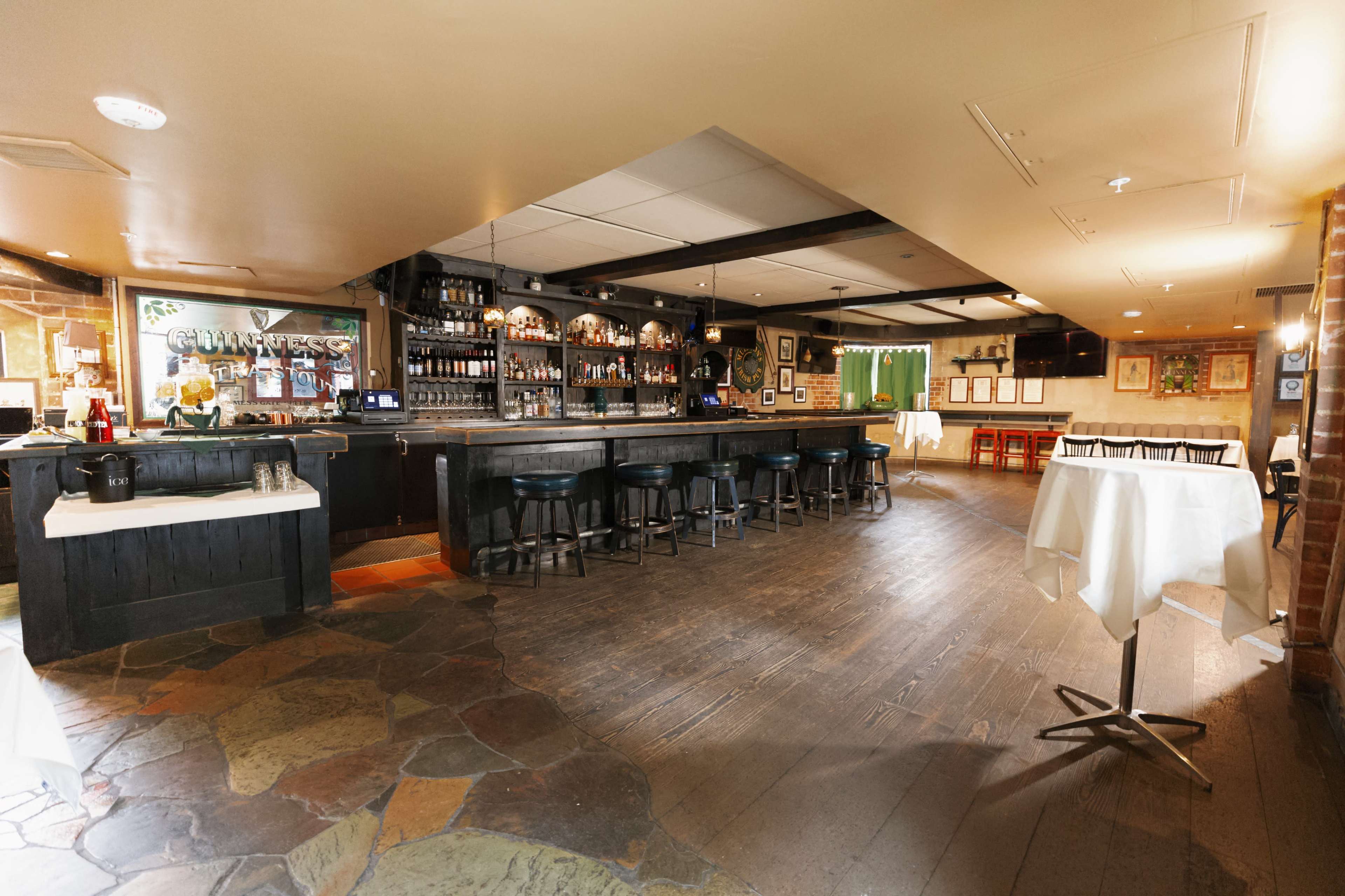 The image depicts an interior view of a bar and dining area with a dark countertop, stools, and wooden flooring.