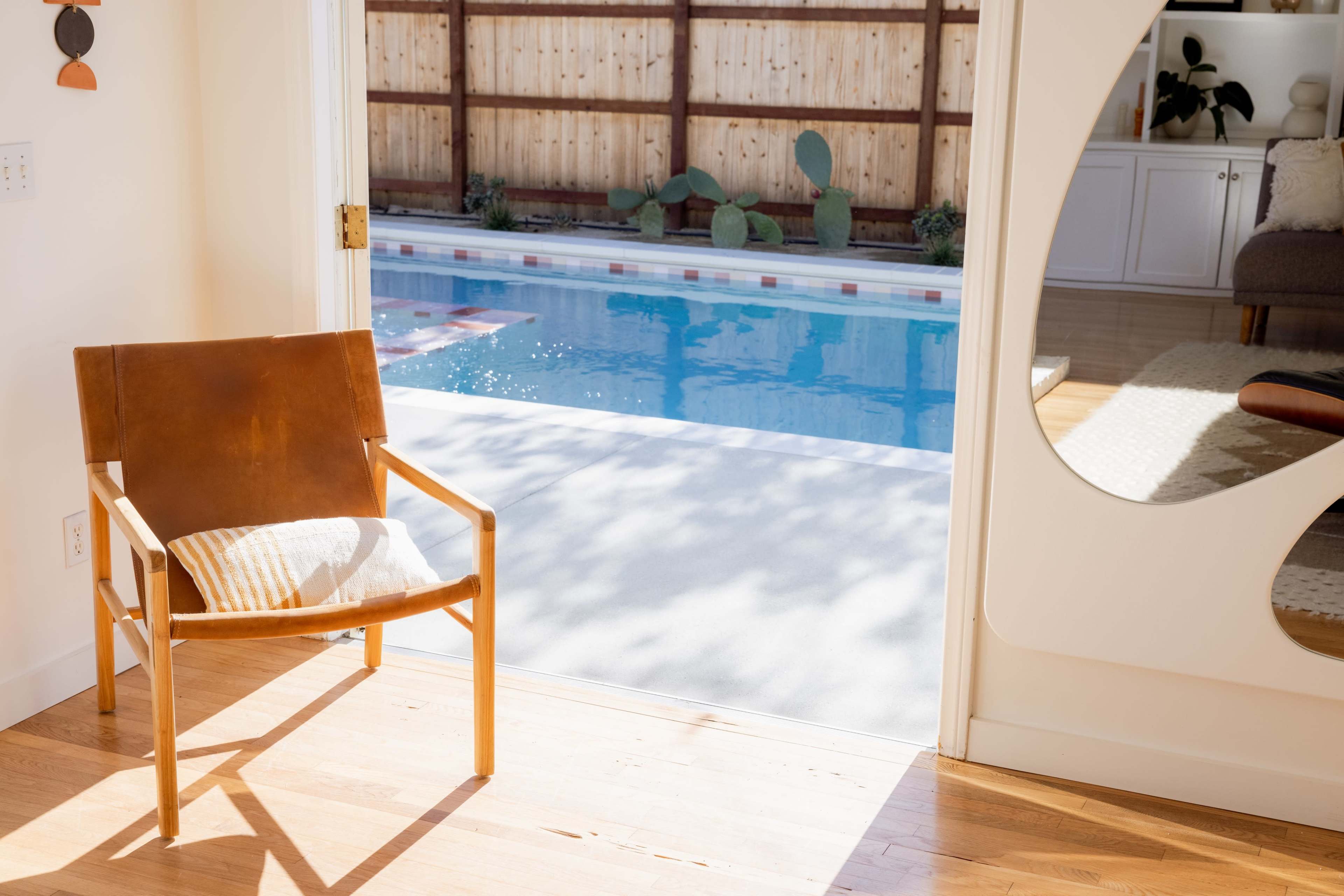 A wooden chair with a cushion faces a swimming pool visible through an open doorway.