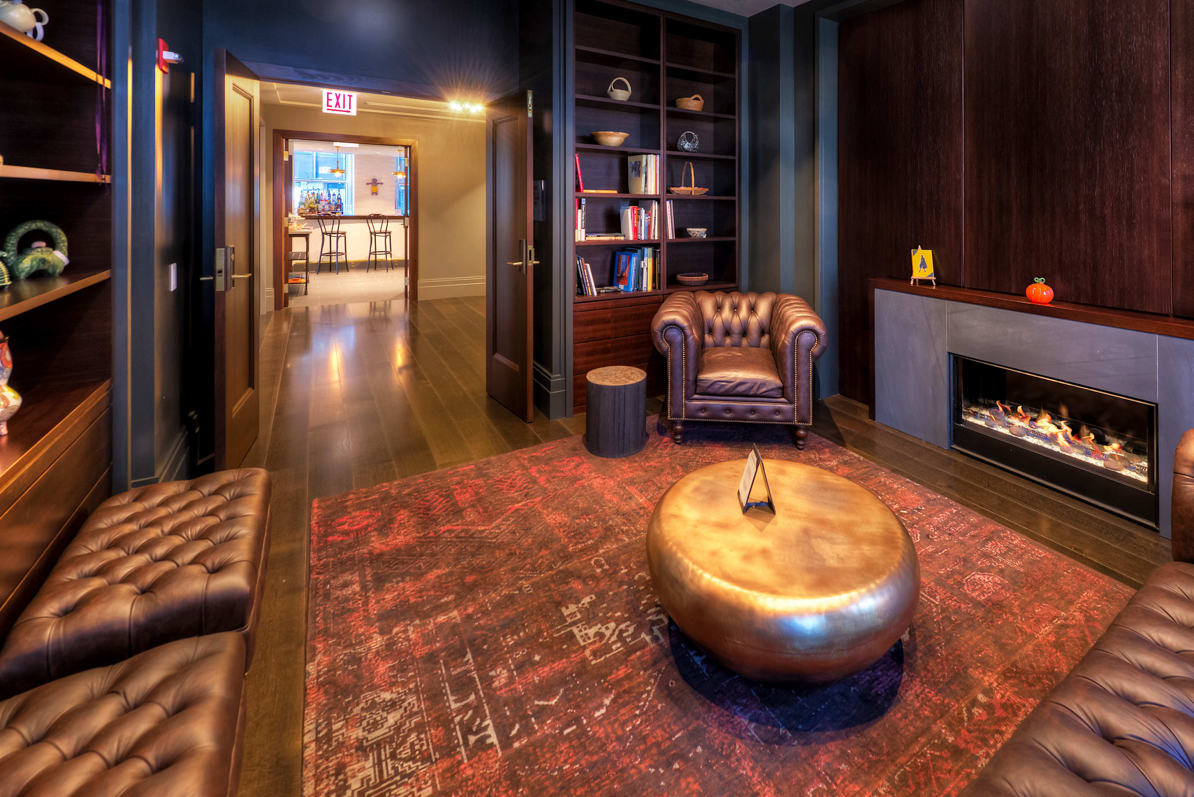 A cozy lounge area features brown leather furniture, a round metallic coffee table, and a fireplace, with a hallway leading to a dining space in the background.