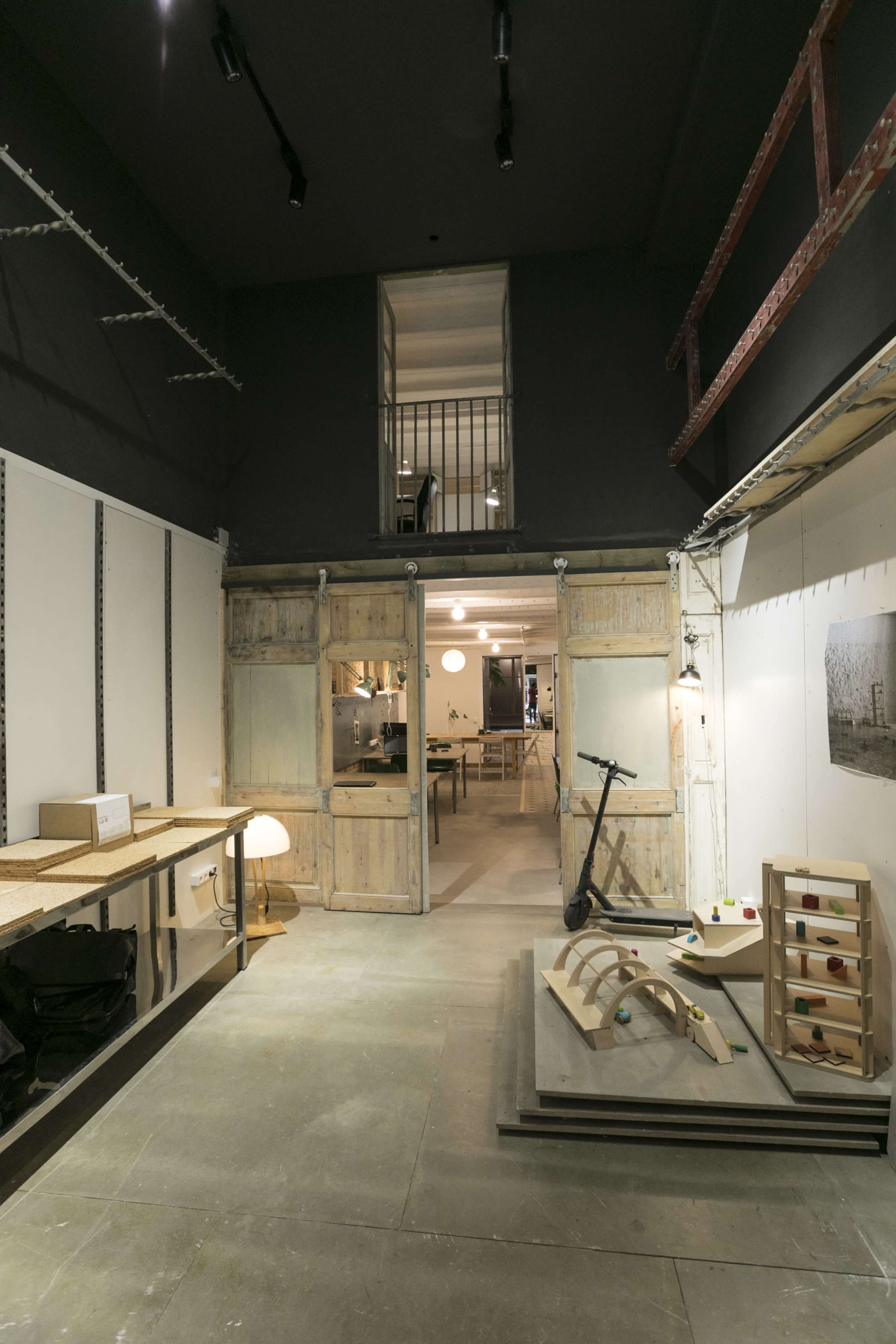 A modern, open interior space featuring wooden sliding doors, a layered wooden floor, and various furniture pieces in a well-lit environment.