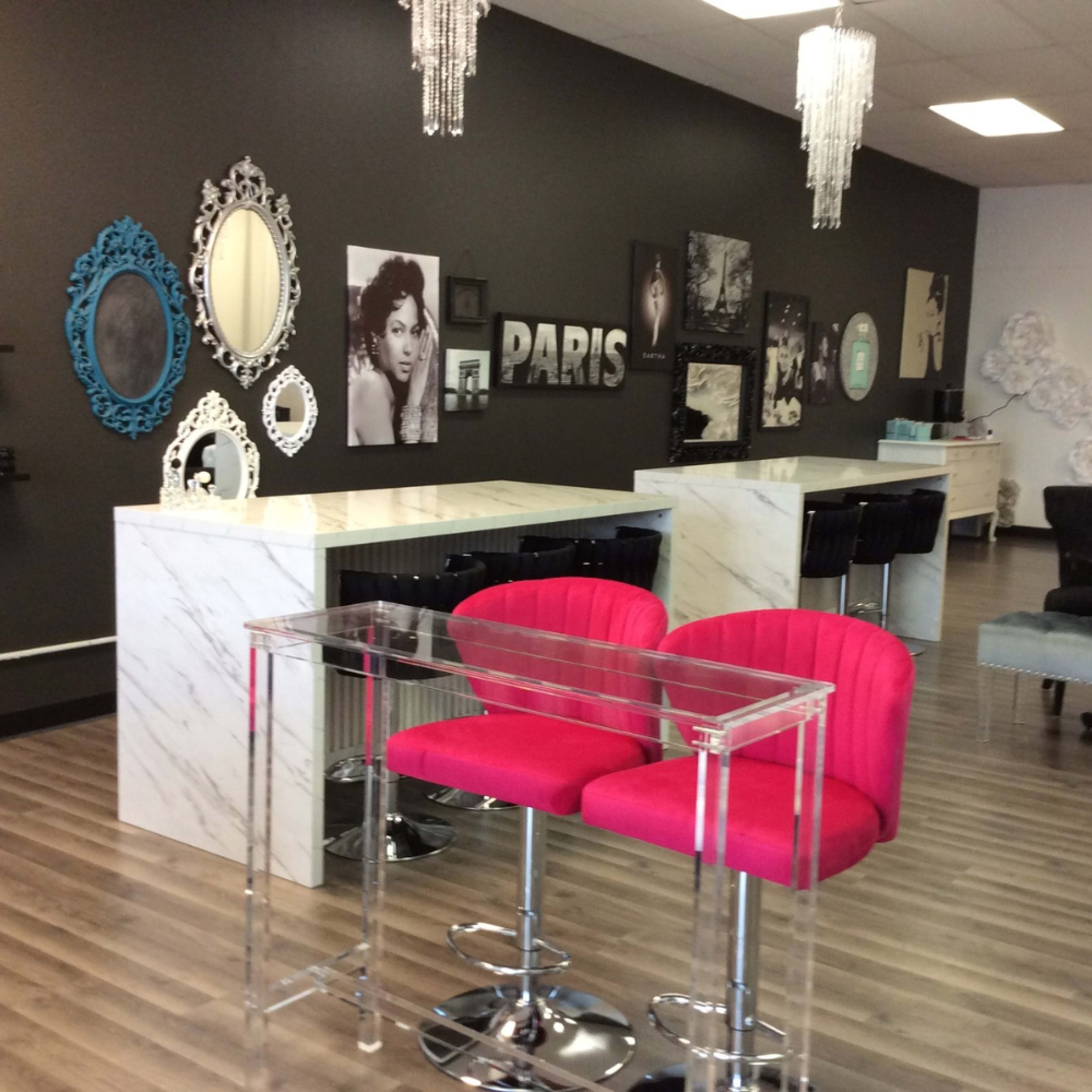 The image shows a modern beauty salon interior with marble counters, pink bar stools, and black-and-white wall art featuring various frames and photographs.