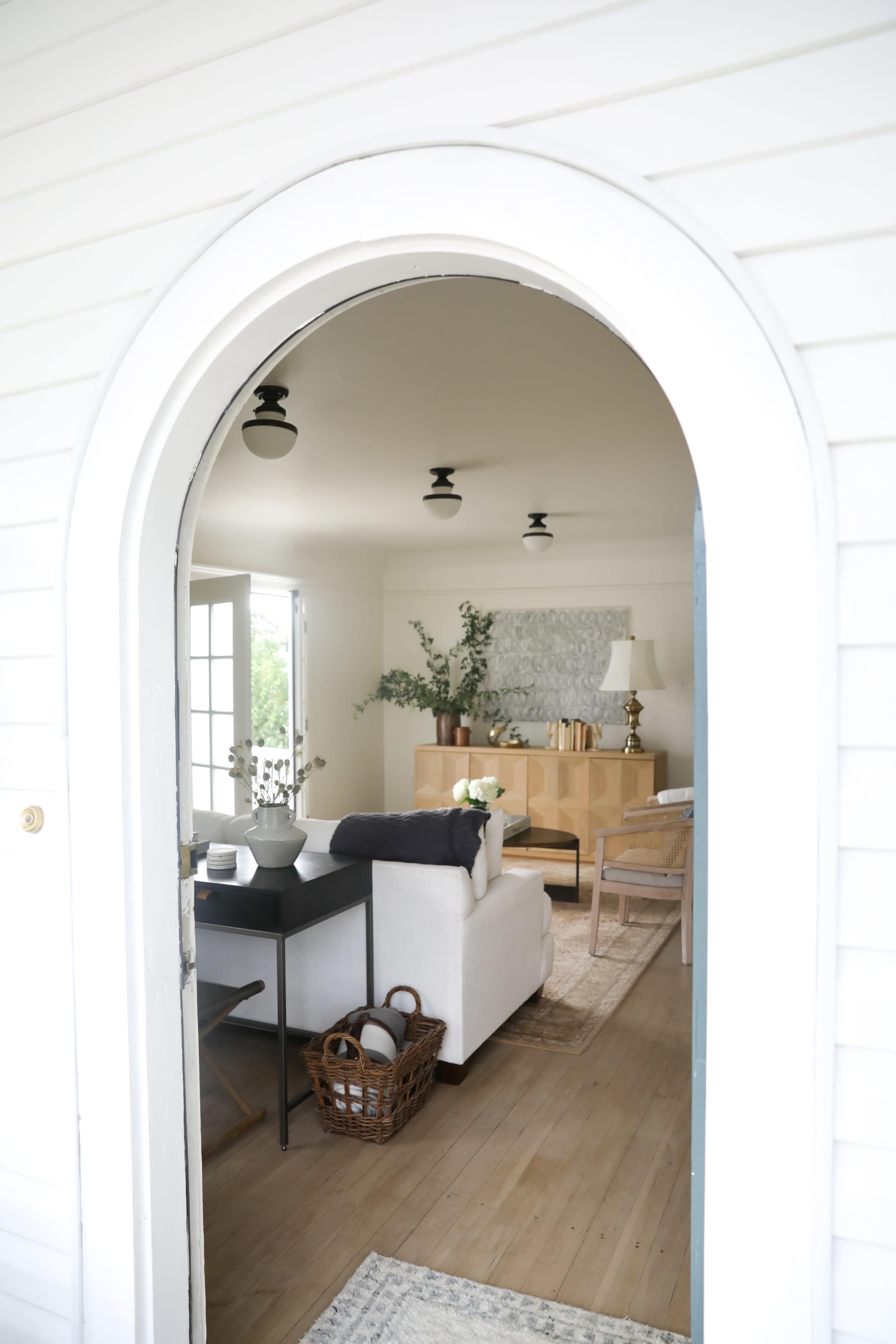 A view of a living room with light-colored furniture and decor seen through an arched entrance.