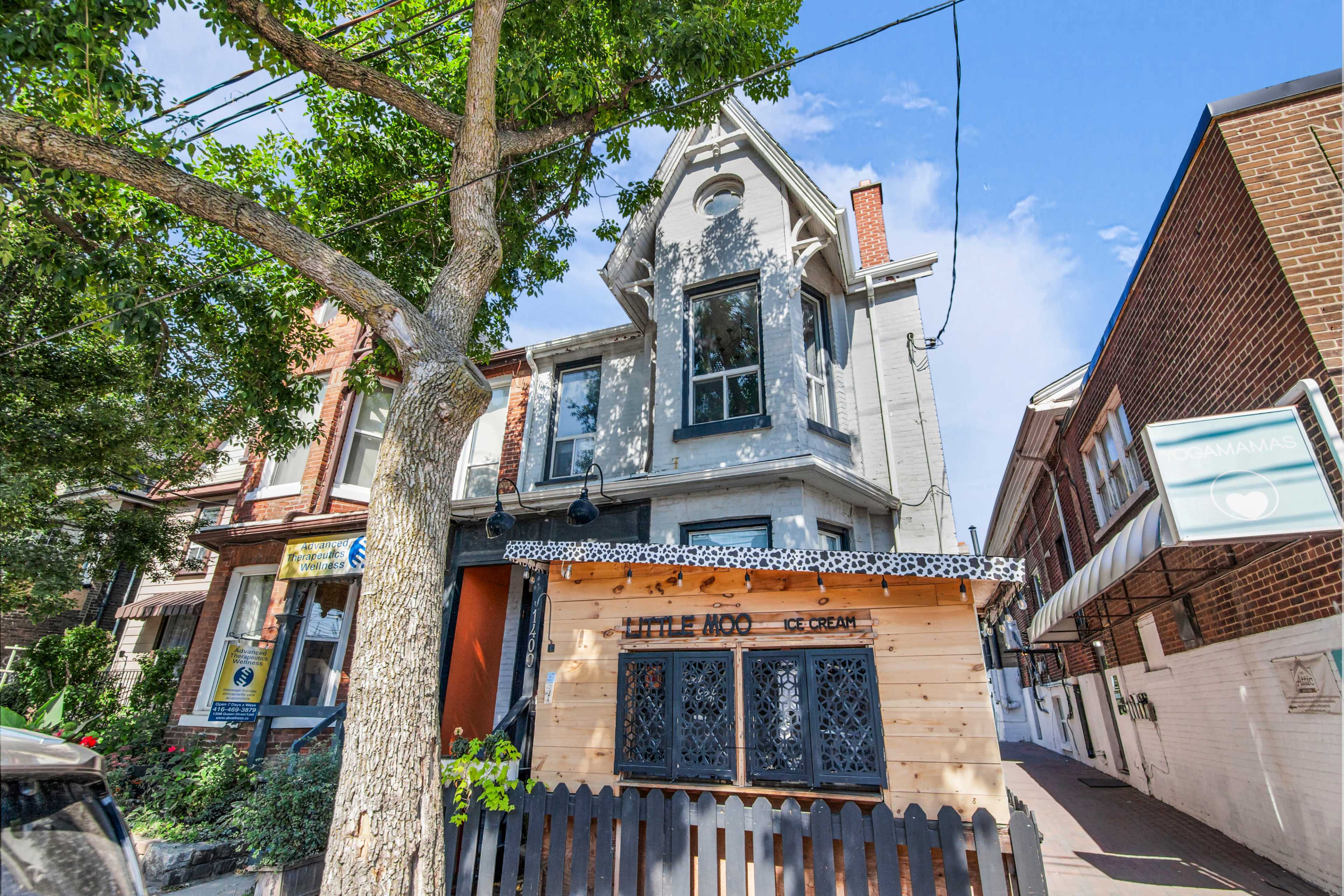 The image shows a two-story gray house with a small ice cream shop structure at the front, surrounded by trees and other buildings.