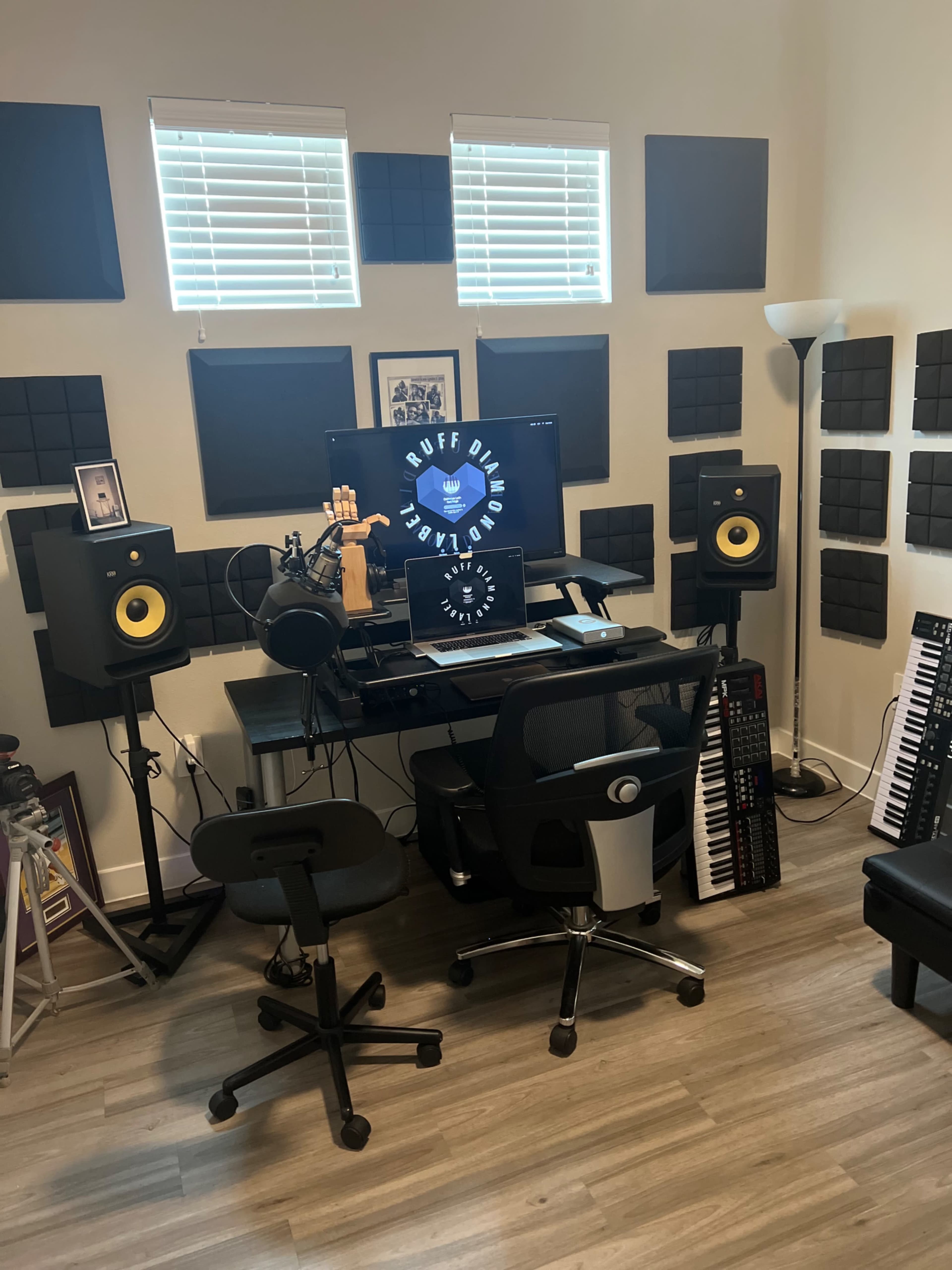 A music studio setup with two monitors, studio speakers, and a variety of musical equipment arranged around a central desk.