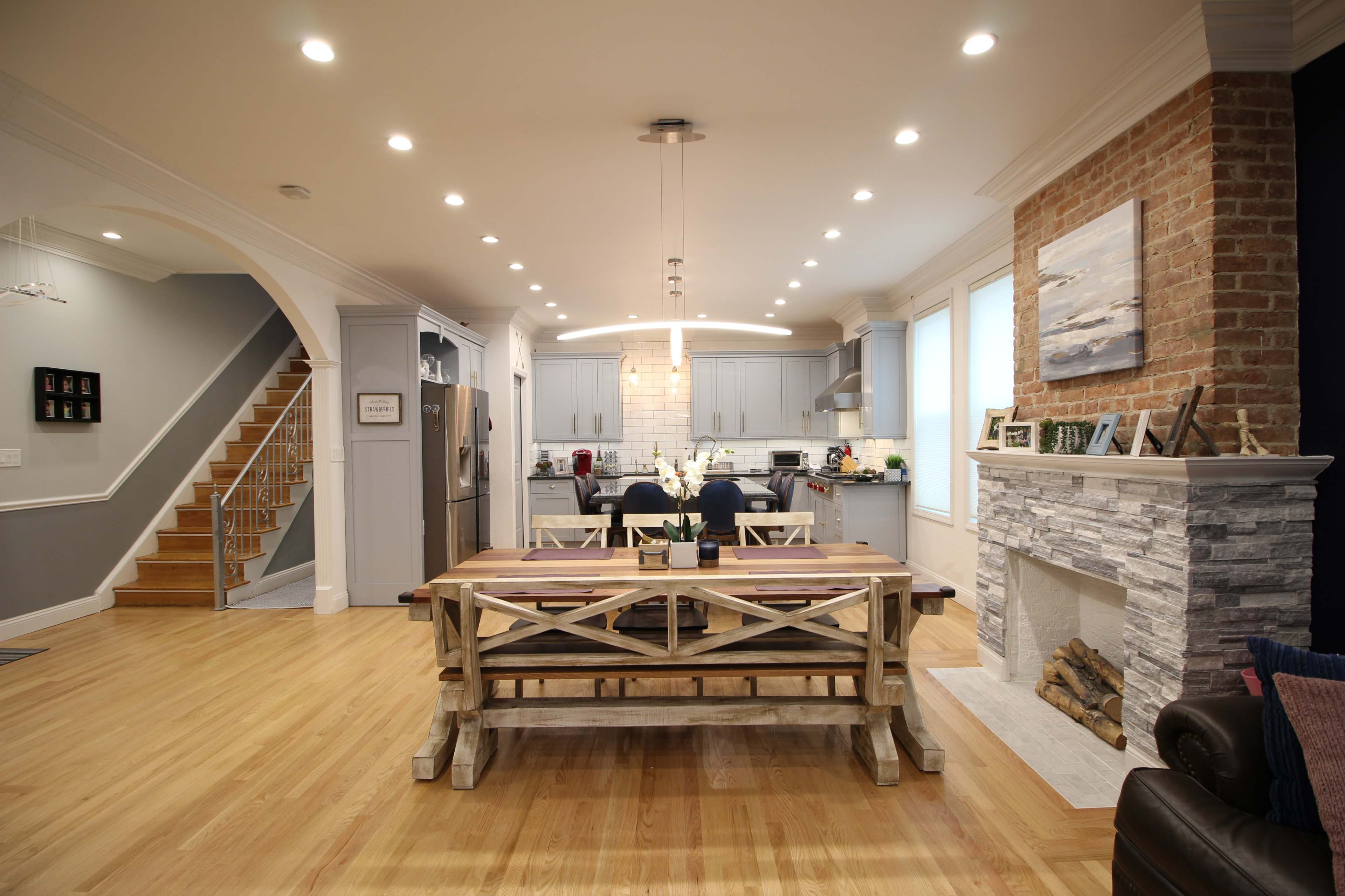 A modern open-concept kitchen and dining area featuring a wooden dining table, brick and stone accents, and a staircase leading to the upper level.