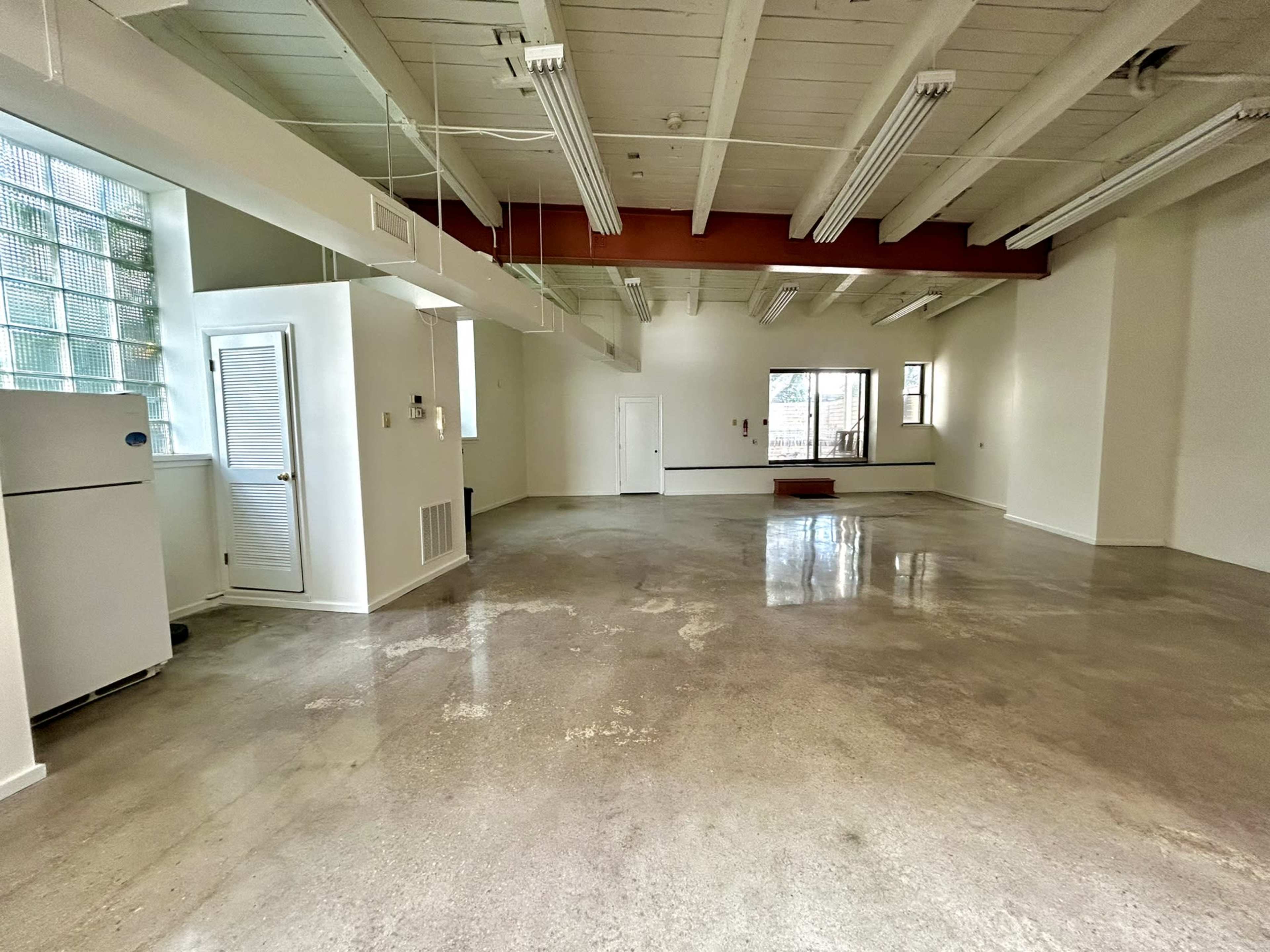 The image shows a spacious, empty room with polished concrete floors, high ceilings, and large windows.