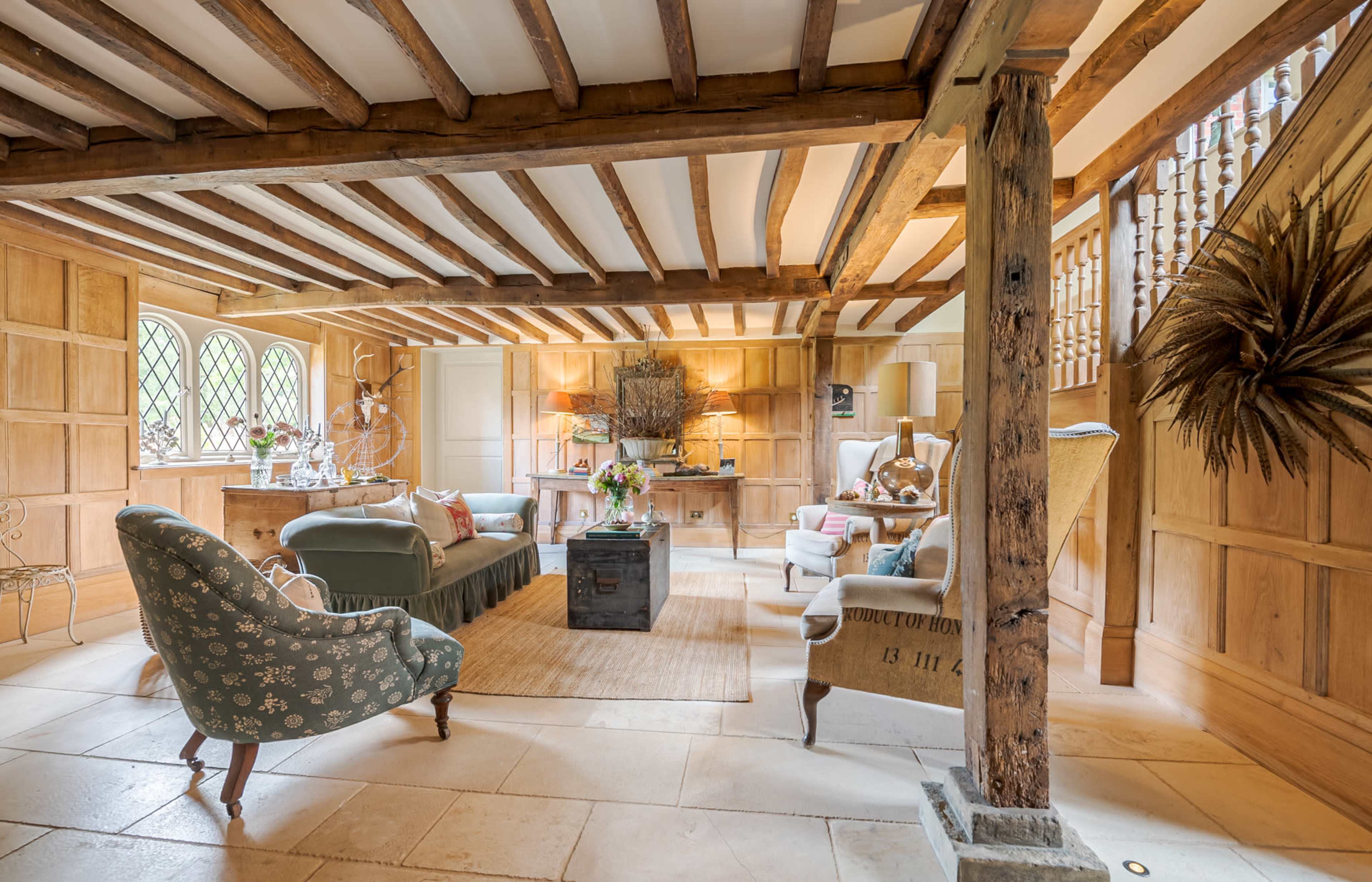 The image shows a spacious living area with wooden beams, a mix of seating arrangements, and a decorative wooden cabinet.