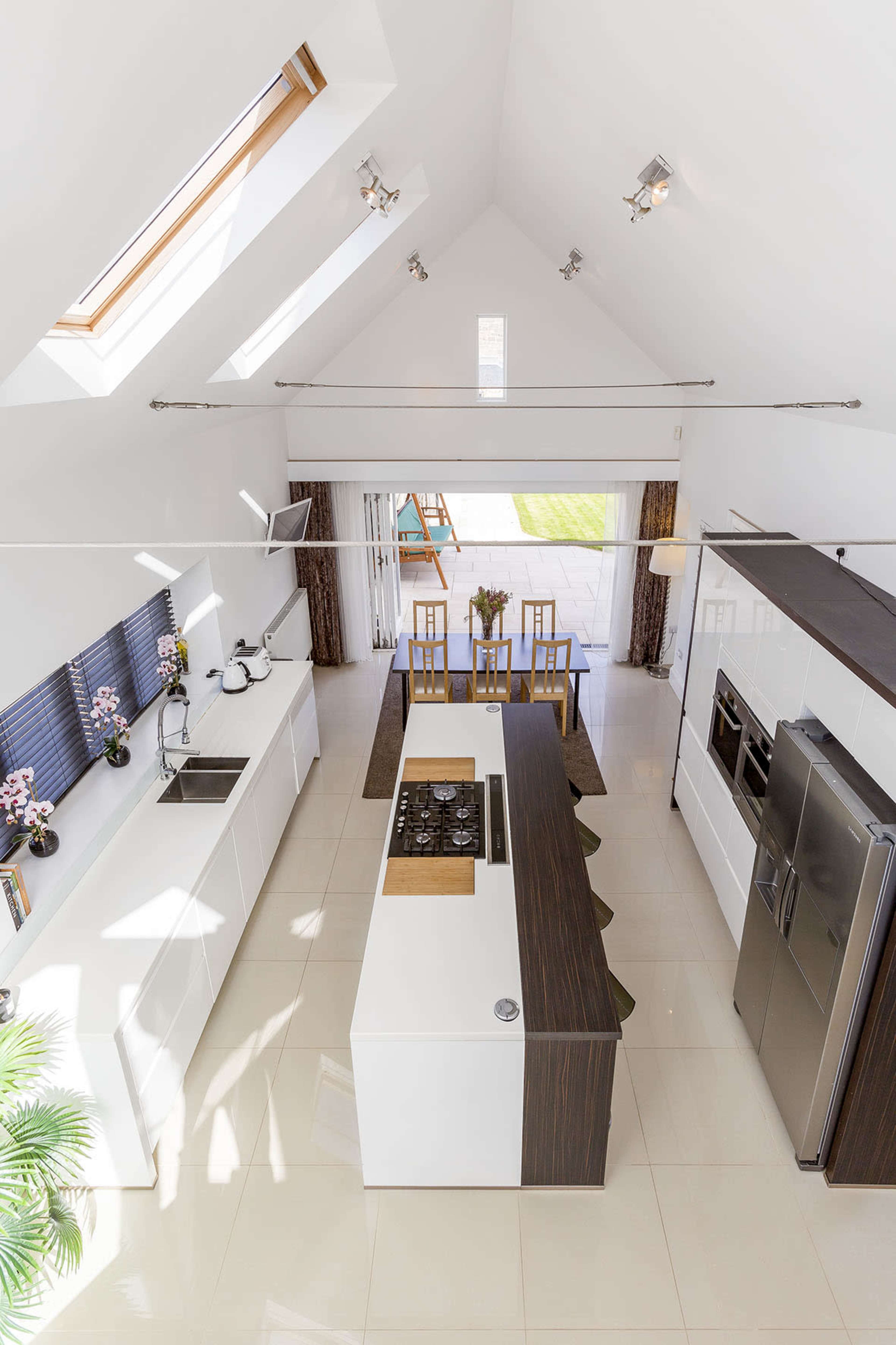 A modern kitchen with white cabinetry, a central island with a cooktop, and a dining area adjacent to large glass doors leading to an outdoor space.