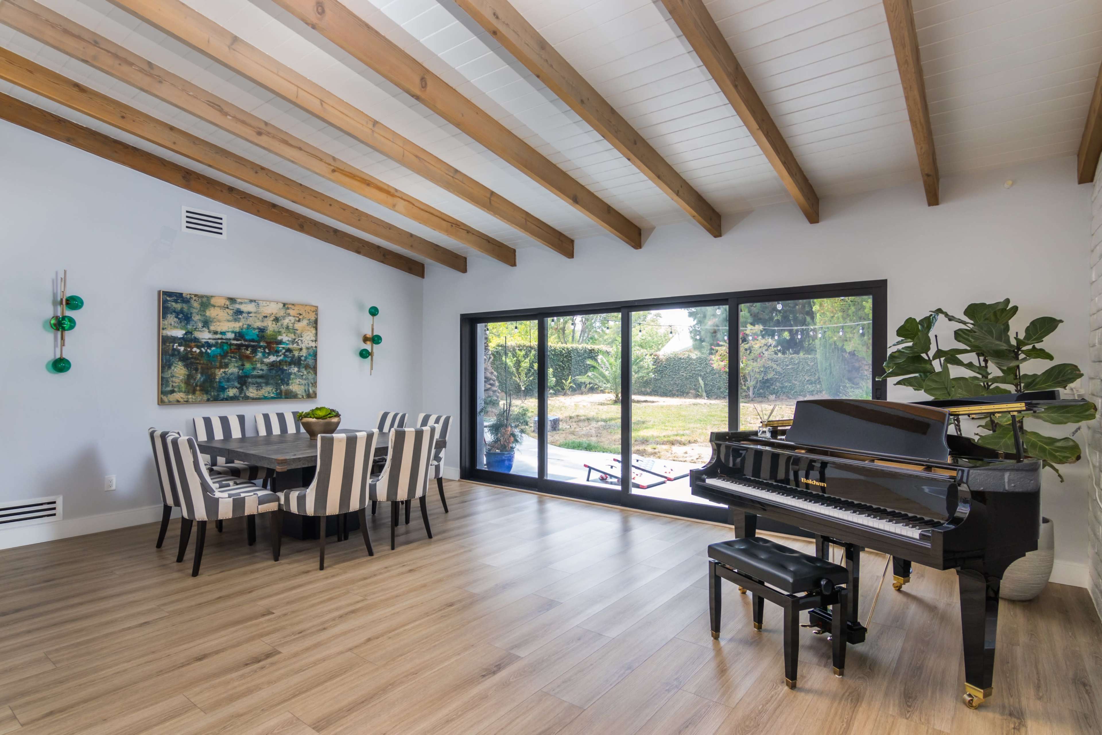 A modern living space featuring a dining area with striped chairs, a grand piano, and large windows overlooking a garden.
