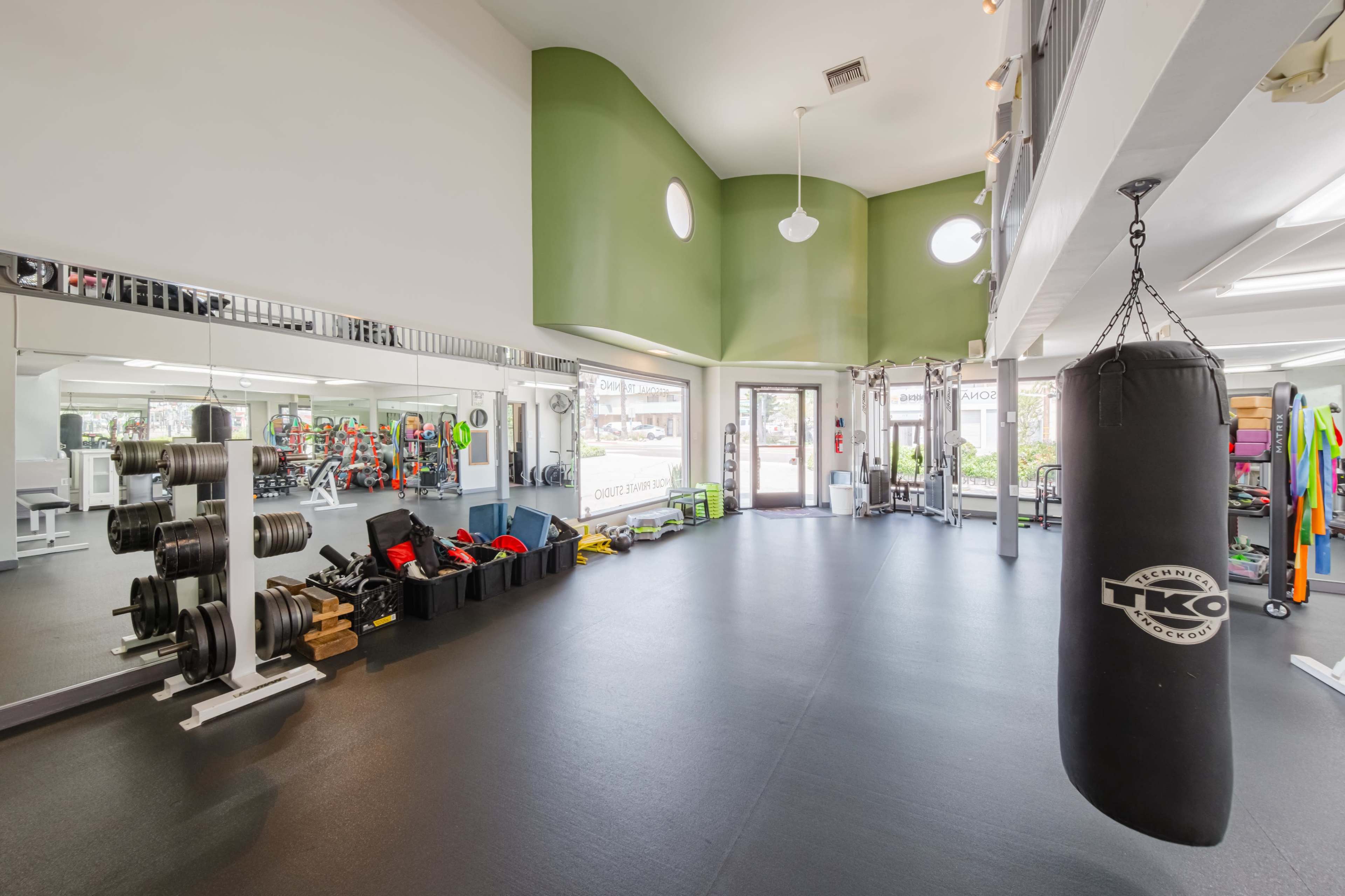 A spacious gym interior featuring weightlifting equipment, a punching bag, and colorful exercise mats arranged neatly along the walls.