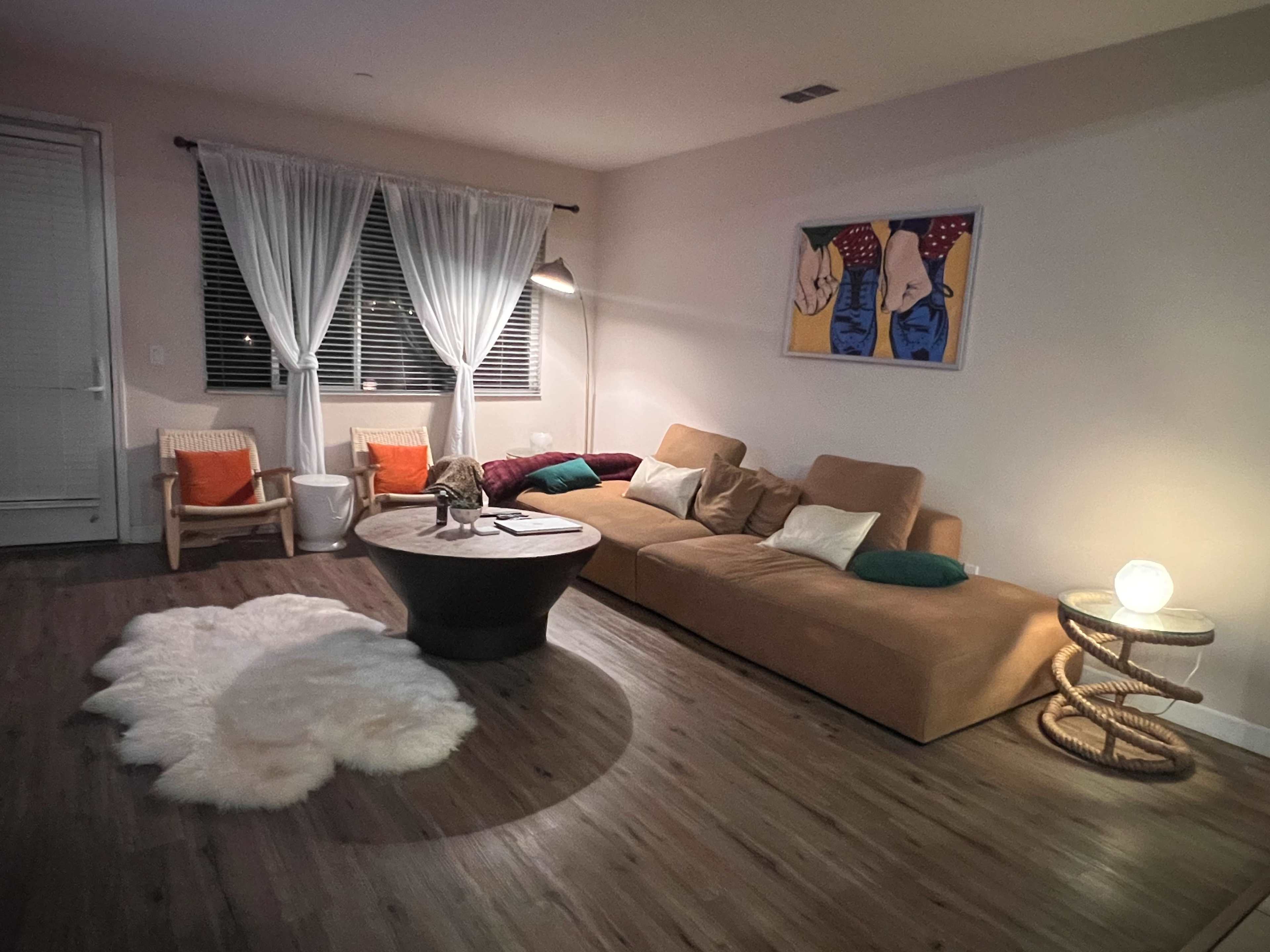A cozy living room with a large sectional sofa, a round coffee table, and a light fixture, surrounded by a decorative rug and art on the wall.