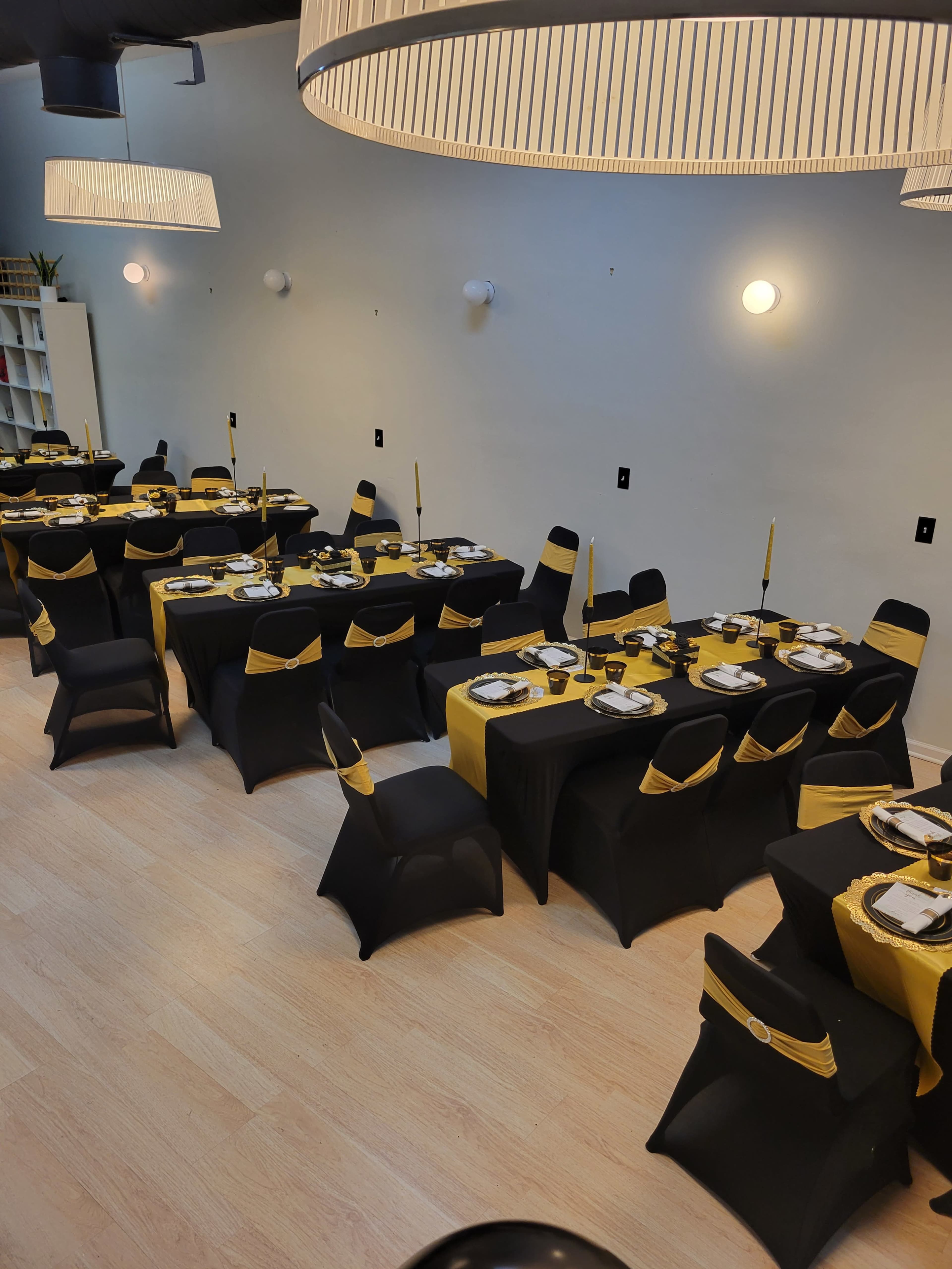 The image shows a dining setup with multiple tables covered in black and yellow tablecloths, adorned with place settings and decorative accents.