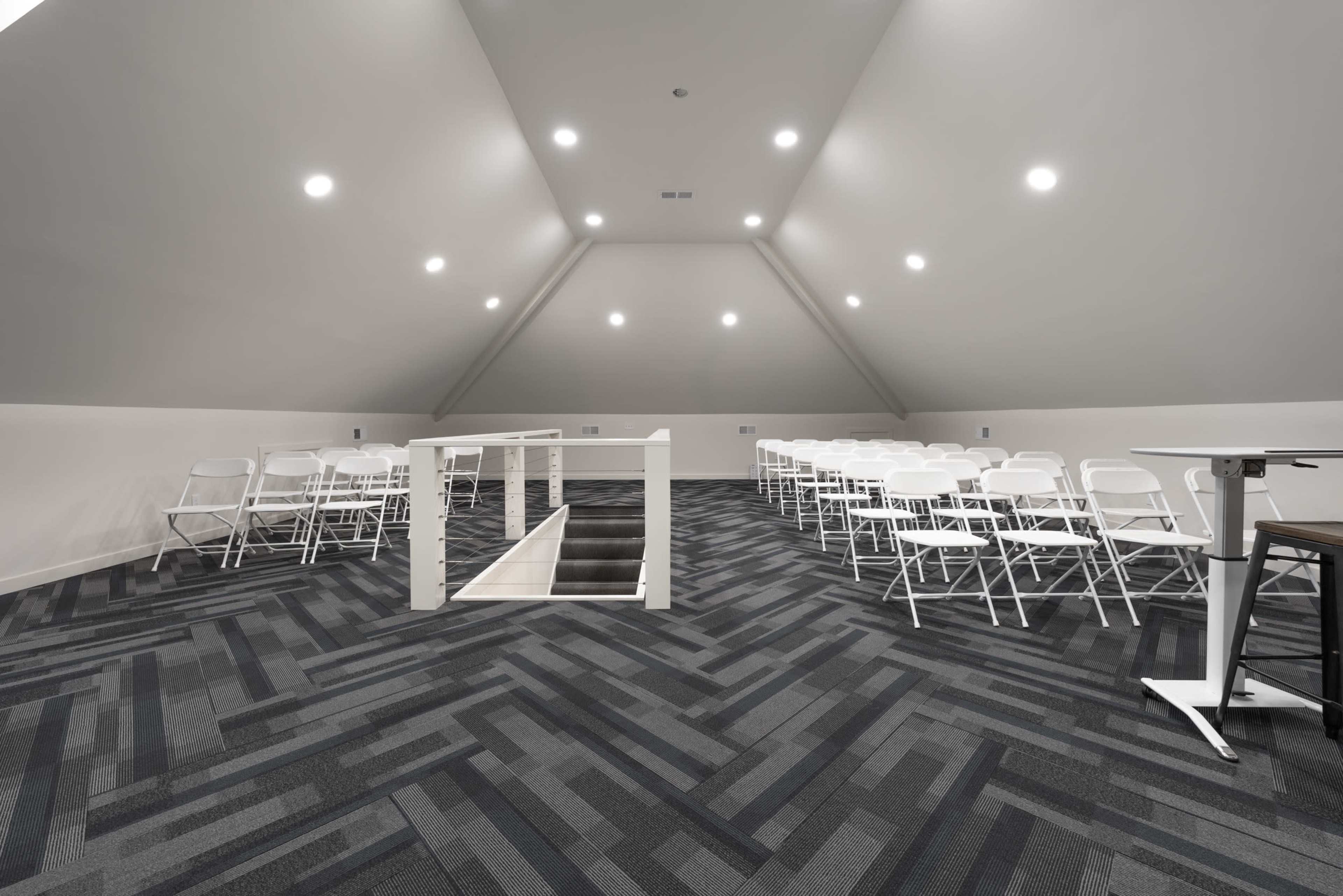 A spacious attic area with rows of white folding chairs arranged for an event, illuminated by recessed lighting.
