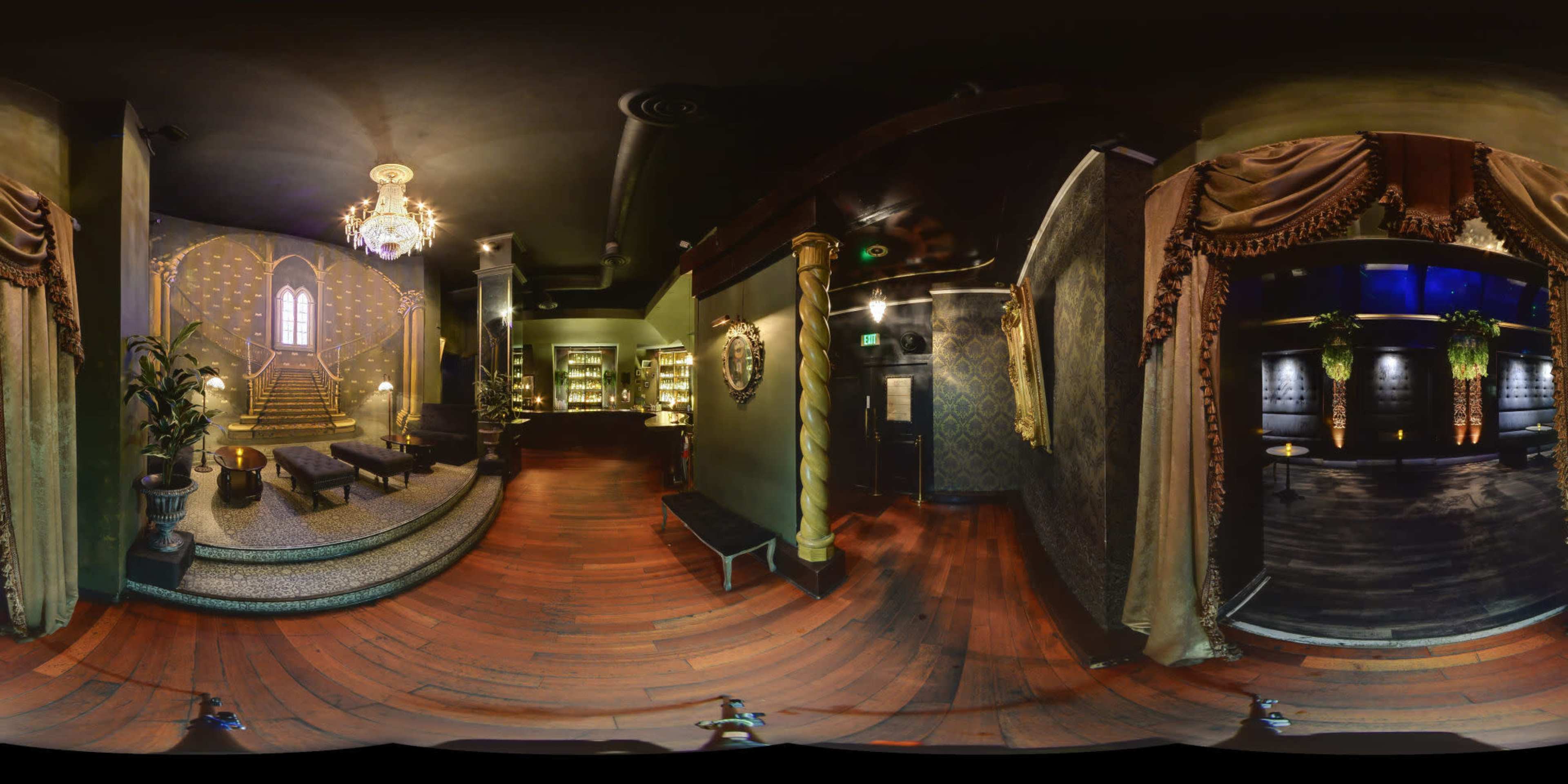 The image shows a luxurious, dimly lit lobby featuring ornate decor, including a chandelier, large mirrors, and a staircase adorned with gold accents.