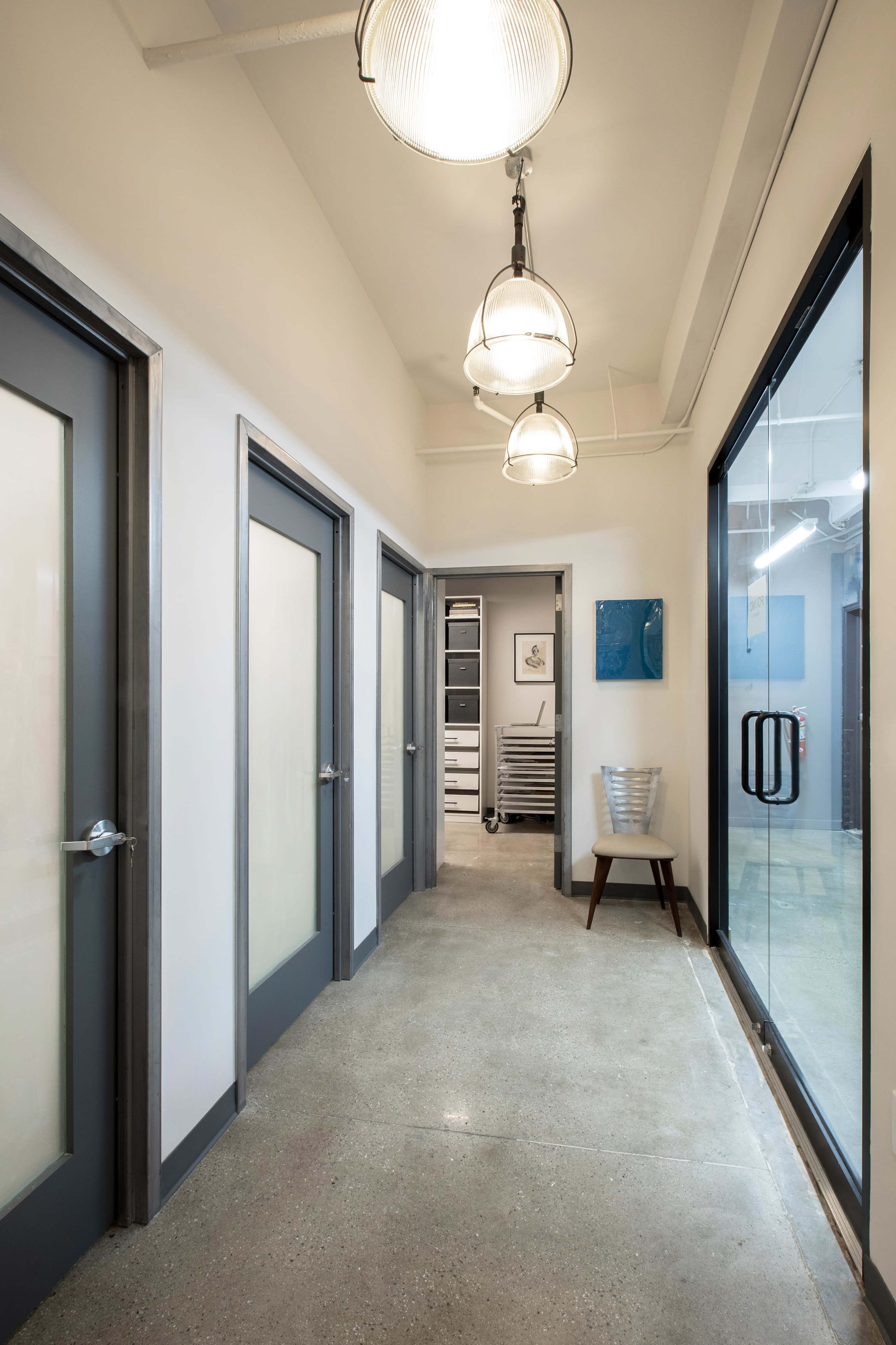 A modern hallway with gray doors on either side and pendant lights hanging from the ceiling.