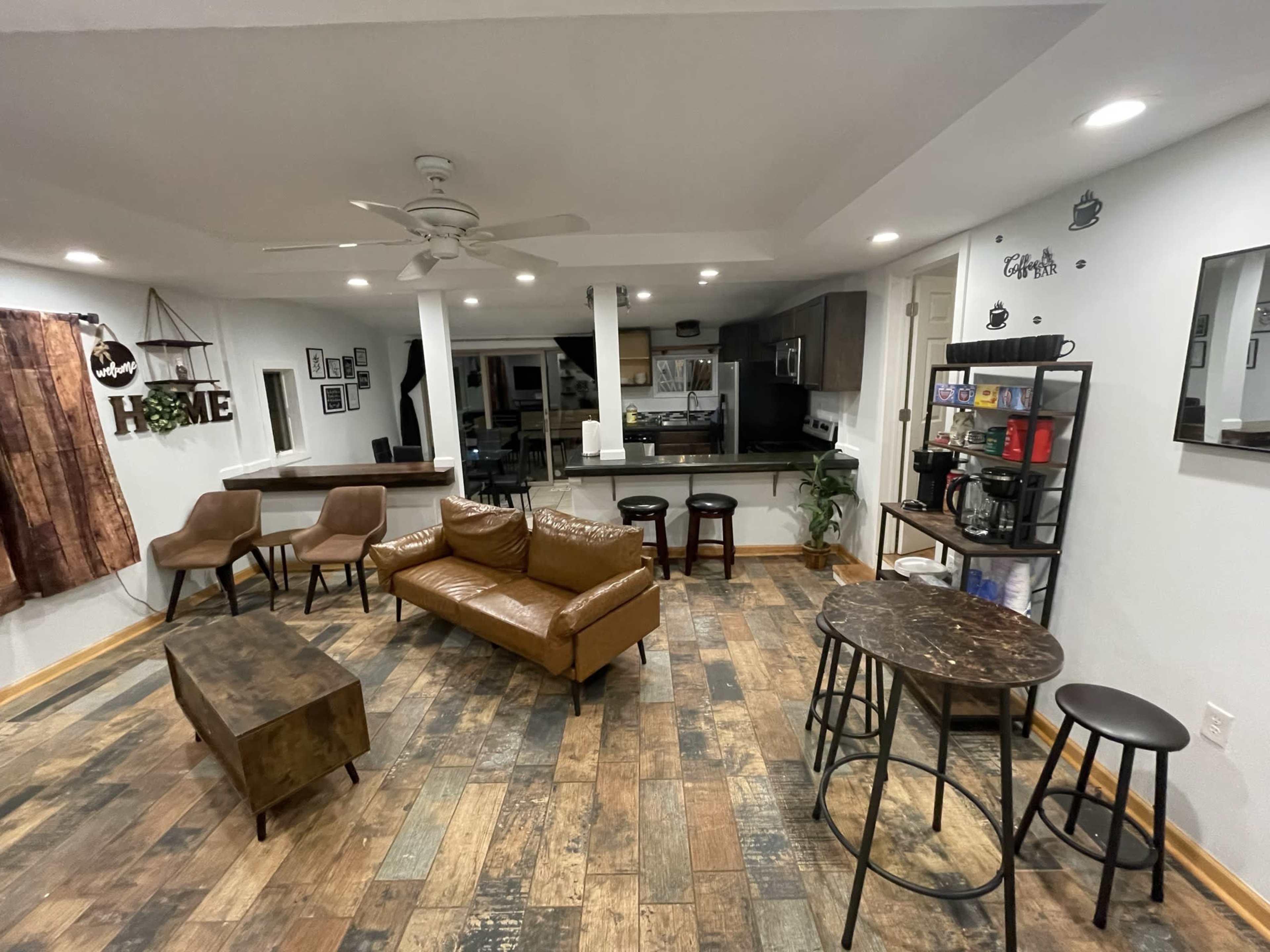 A modern living space with a leather sofa, wooden coffee table, bar stools, and a kitchen area in the background.