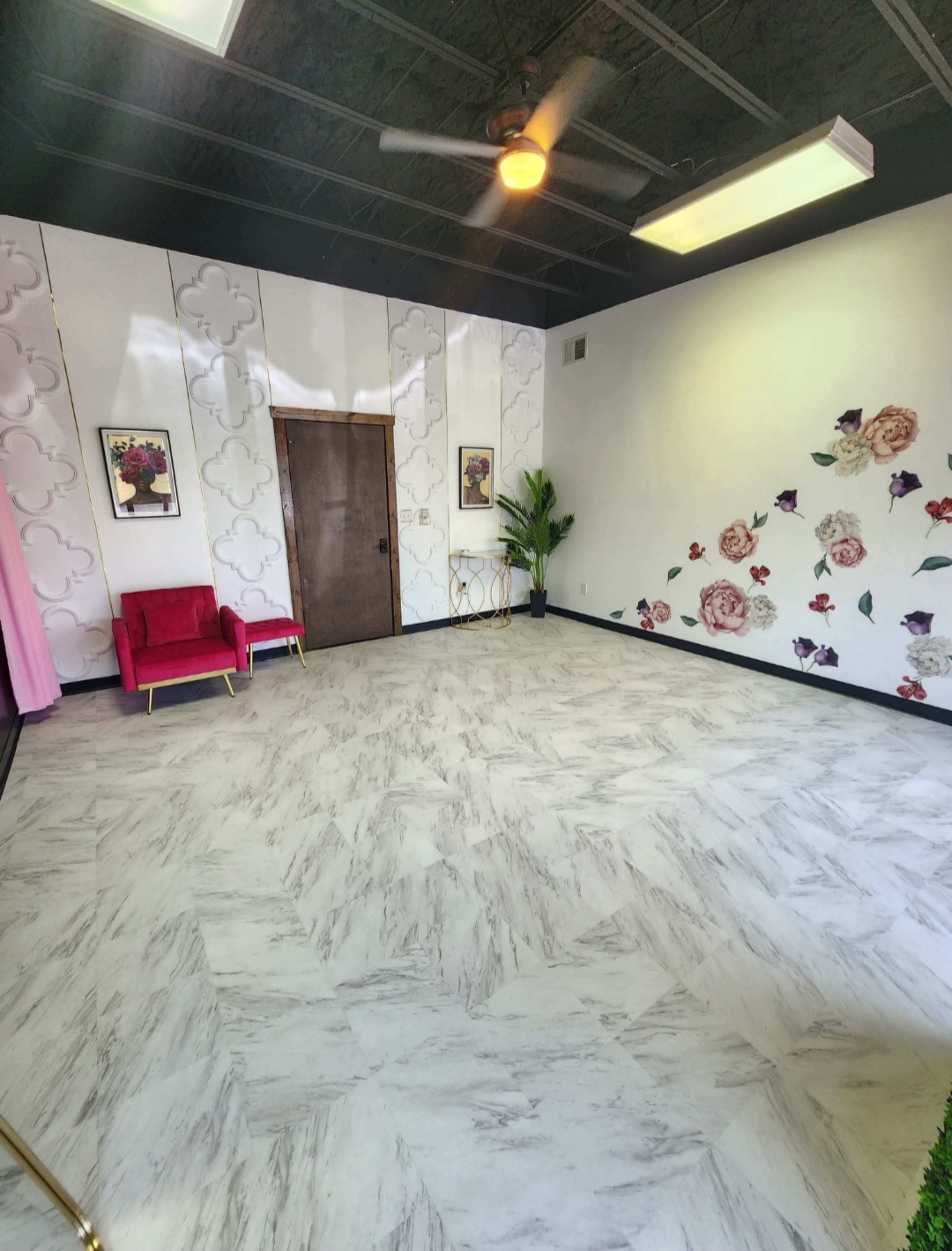 An empty room with light-colored marble flooring, floral wall decor, a wooden door, and a red velvet chair.
