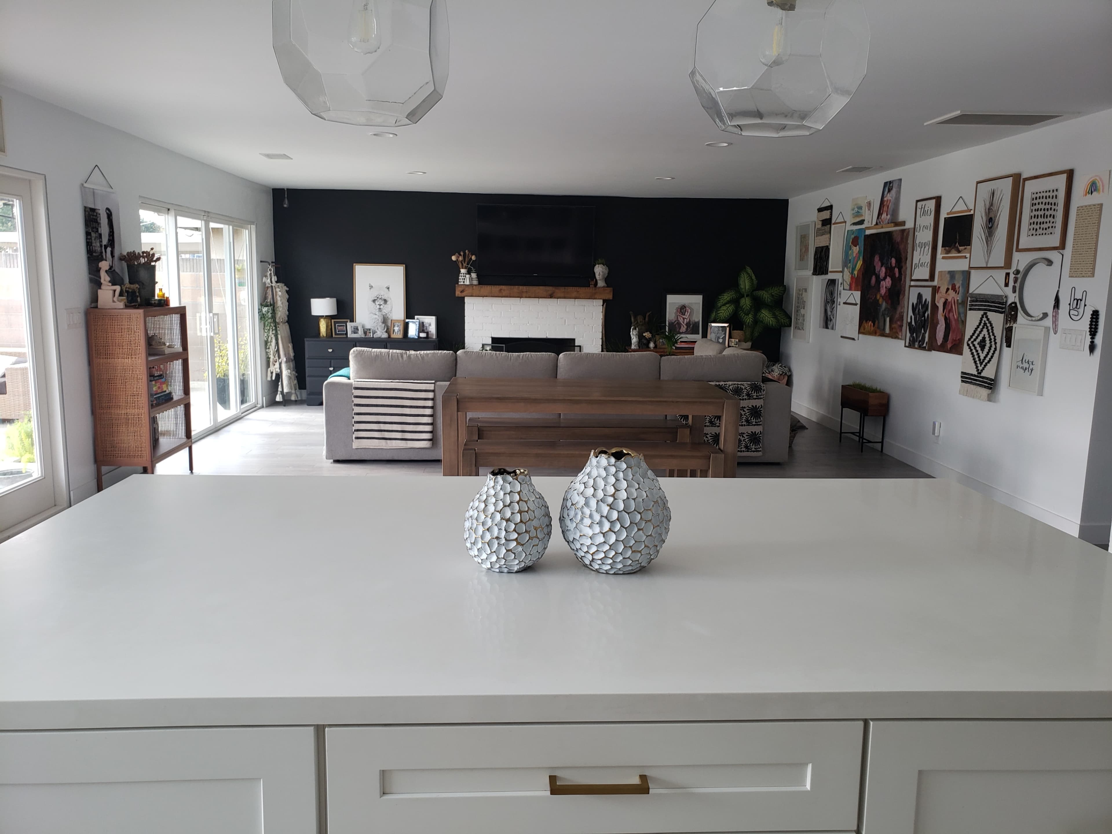 A modern living space features a kitchen island with decorative vases in the foreground and a cozy seating area with artwork on the walls in the background.