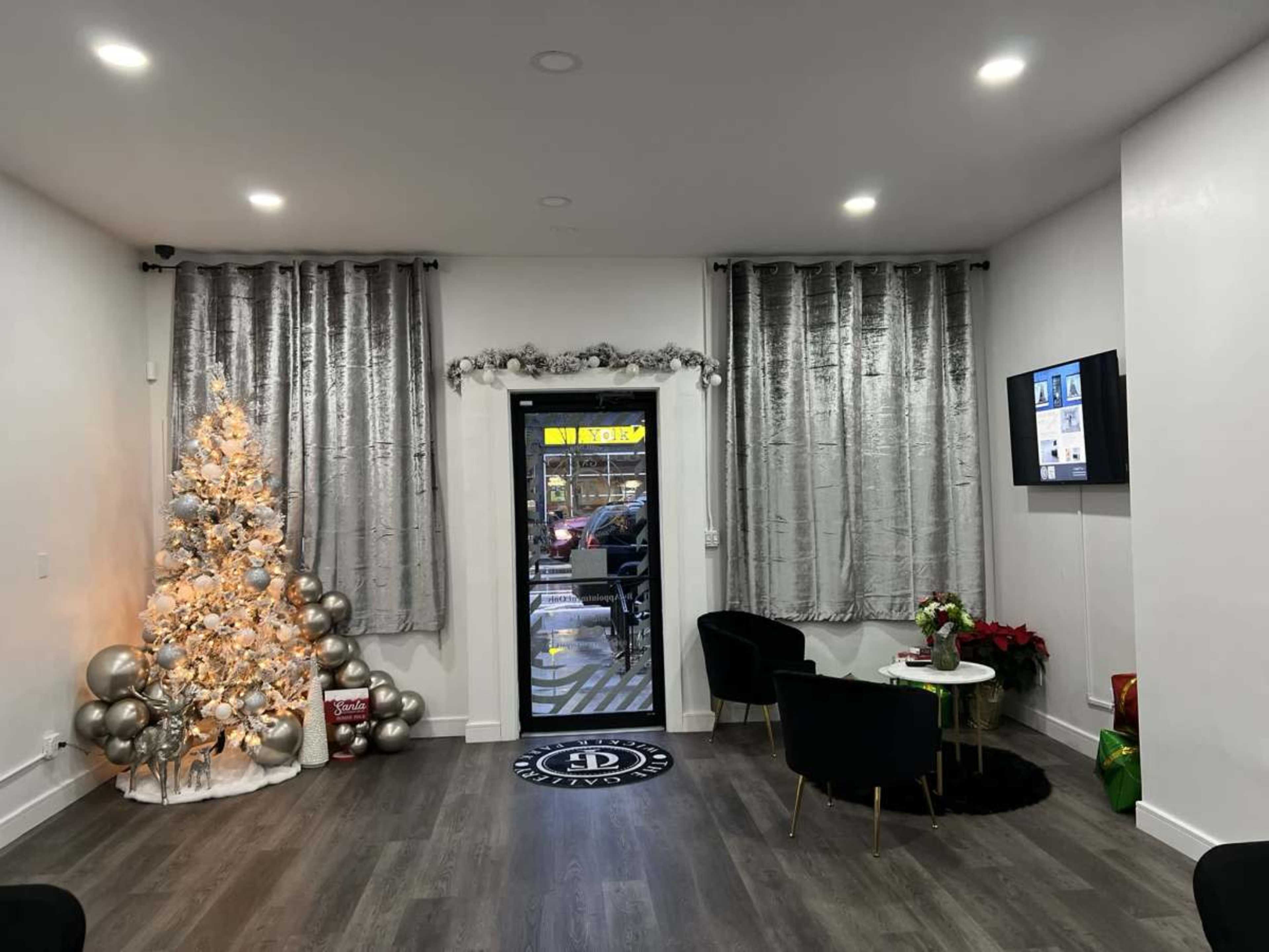 A modern room with a decorative Christmas tree, two black chairs, a small table, and a doorway leading outside.