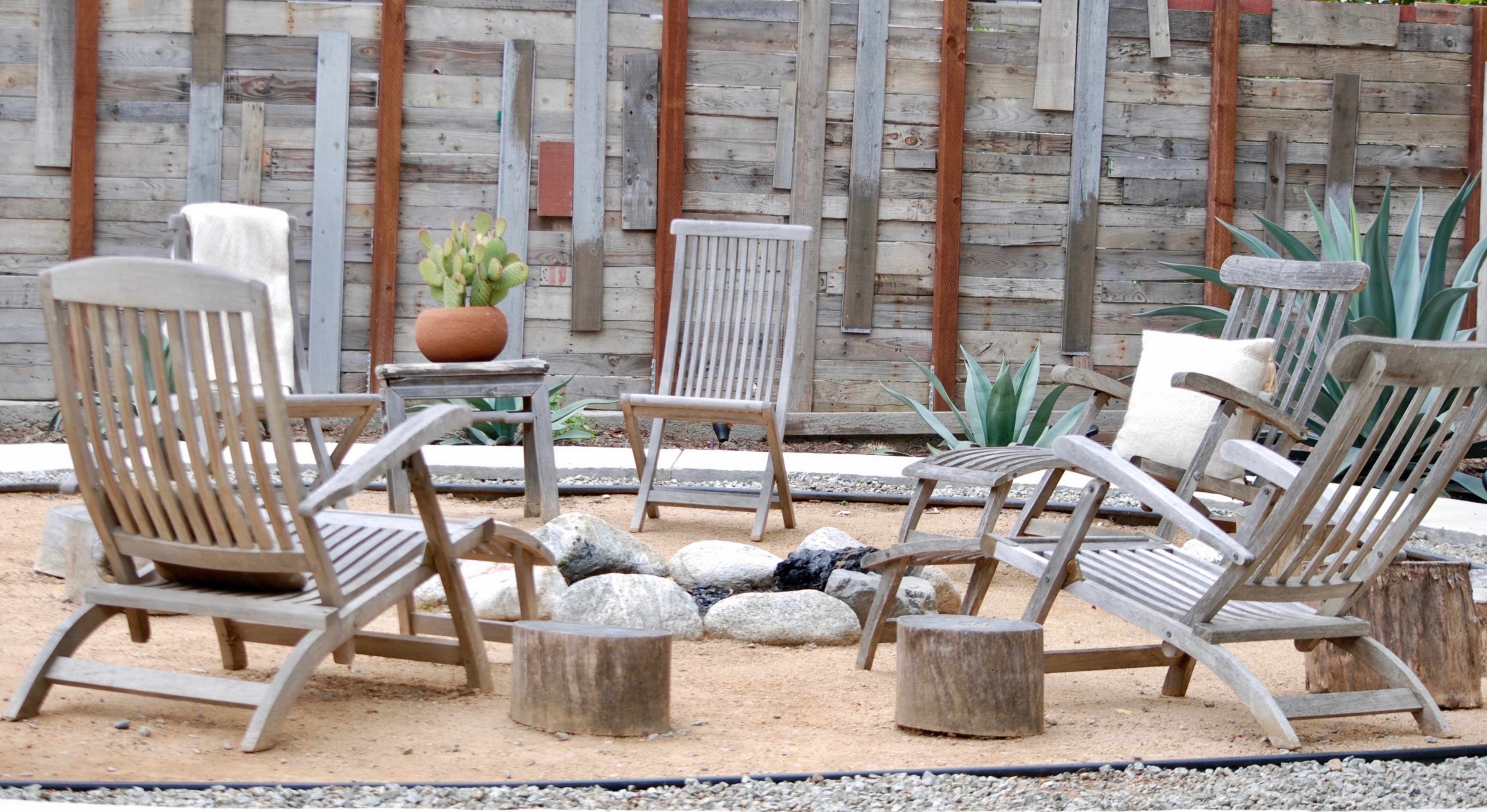 A circle of wooden chairs arranged around a fire pit in a landscaped yard with gravel and plants.
