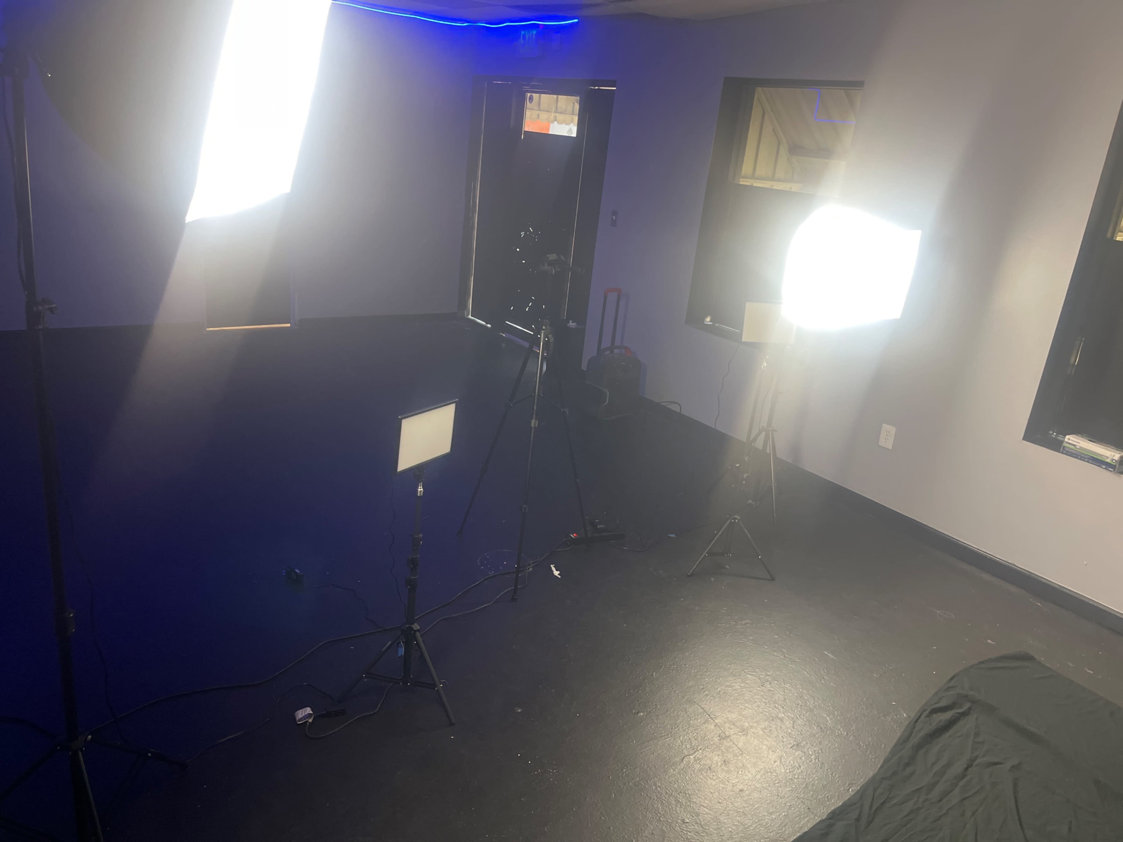 A dimly lit room with three light fixtures set on tripods, illuminating a dark floor and a large black cloth.