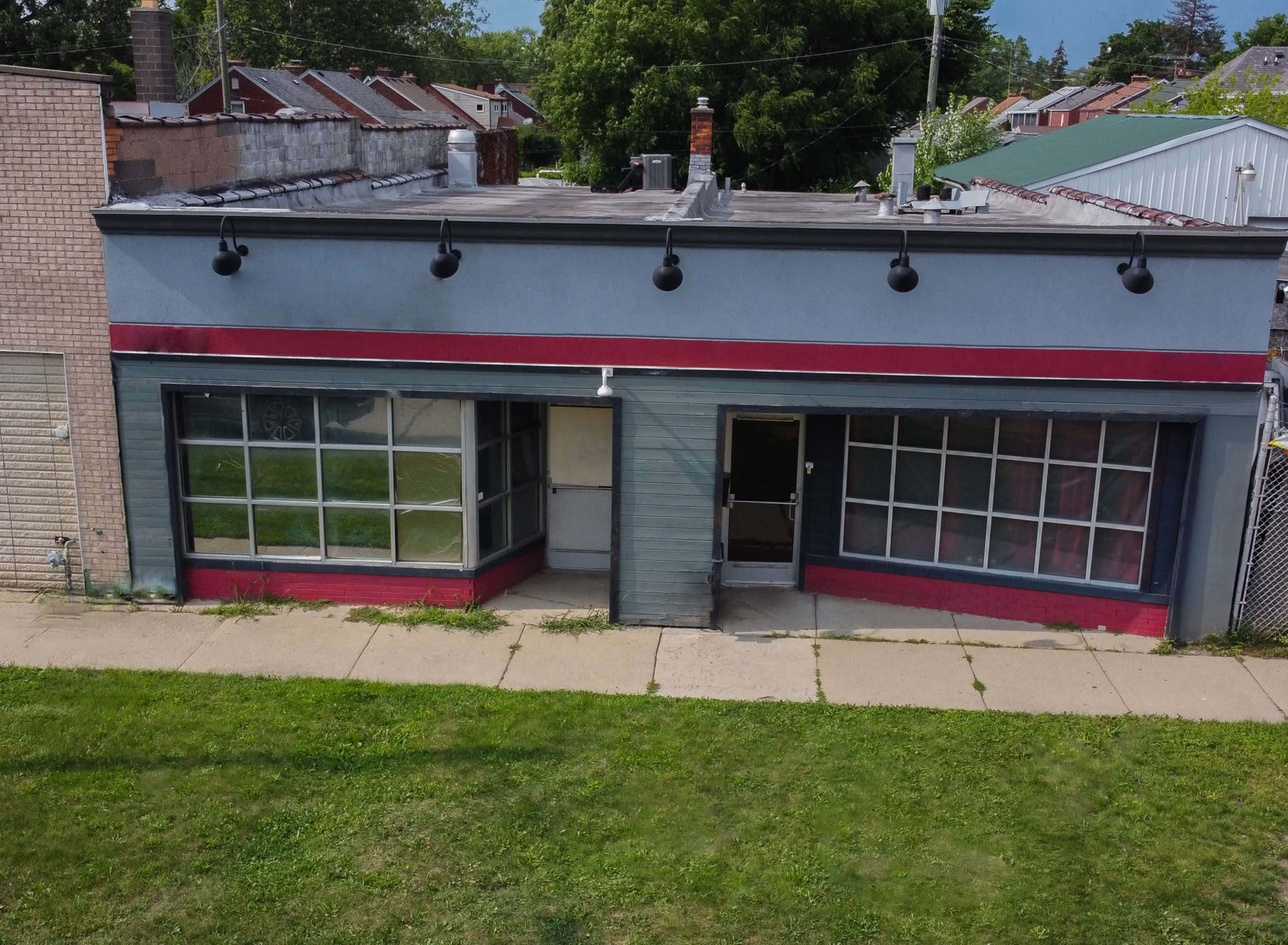 A gray building with large front windows and a red stripe along the top, situated on a grassy area.