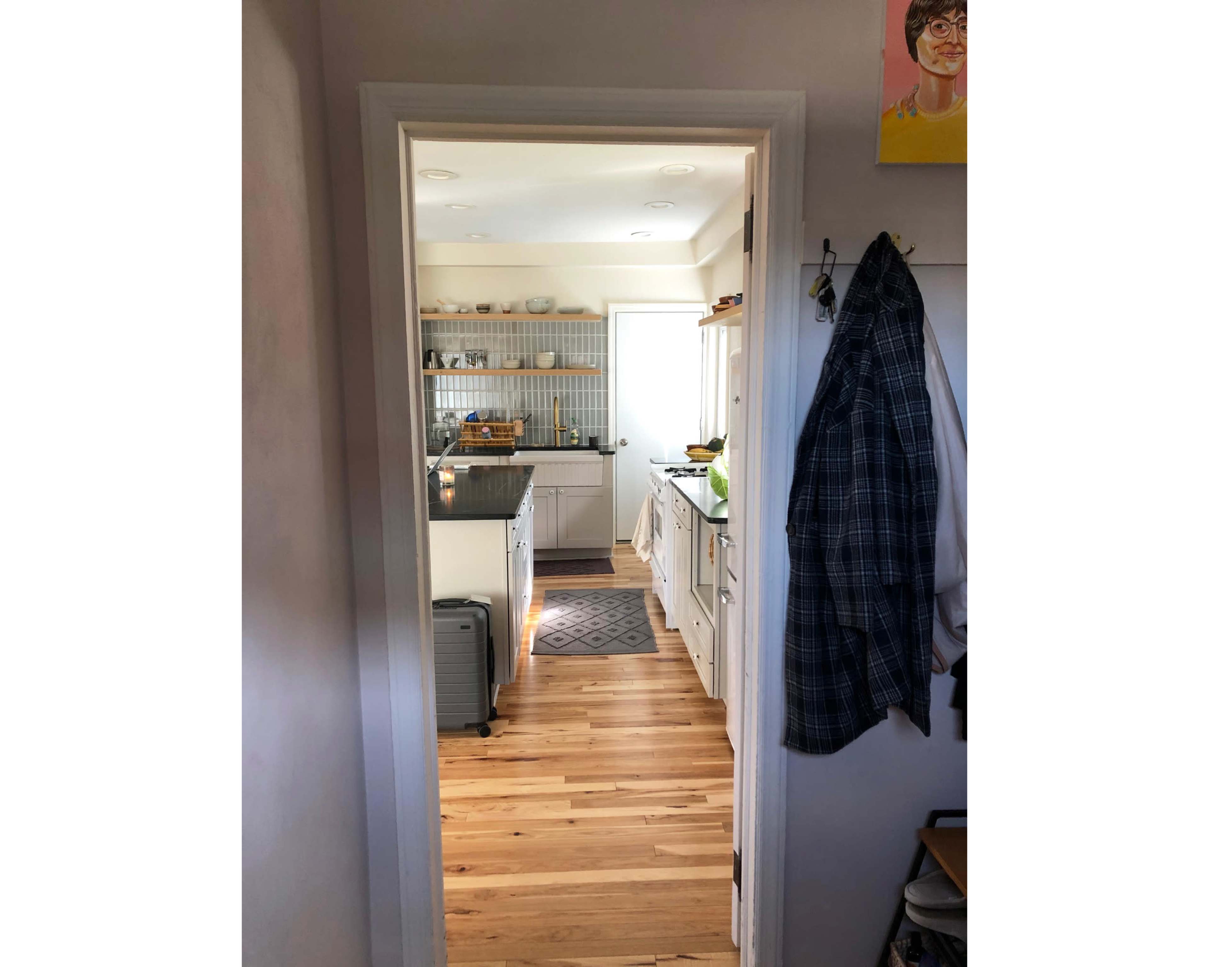 A doorway leads into a brightly lit kitchen with wooden floors, white cabinets, and a visible dining area.