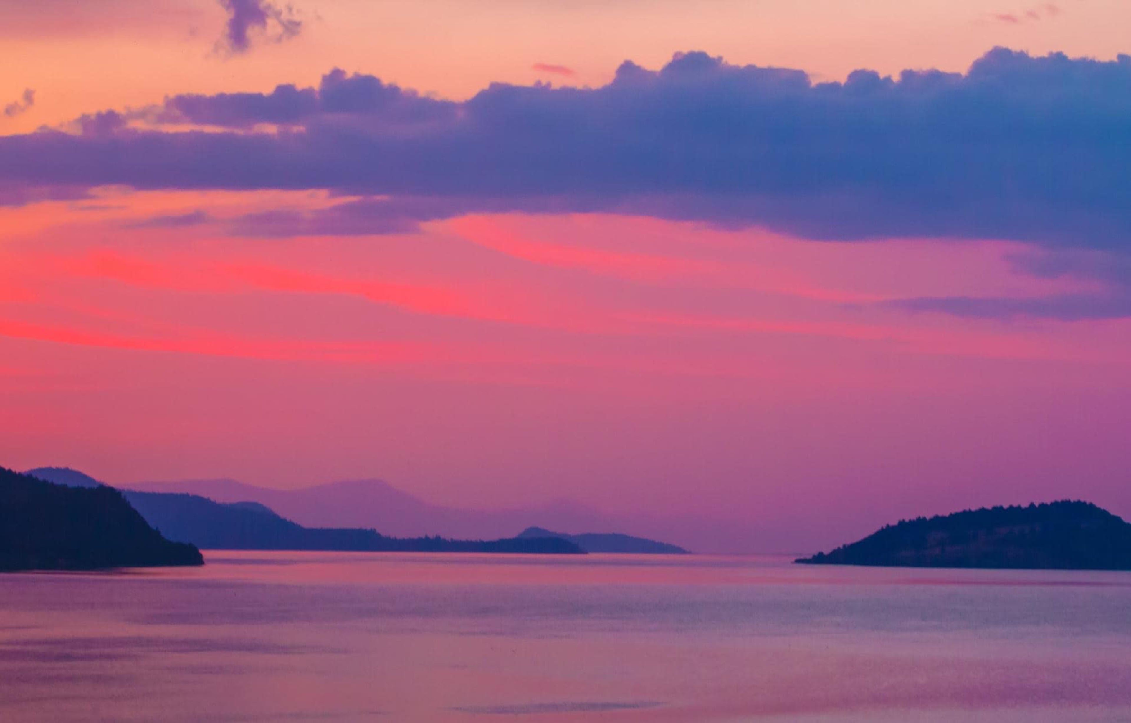 A serene body of water at dusk, with distant islands silhouetted against a colorful sky.