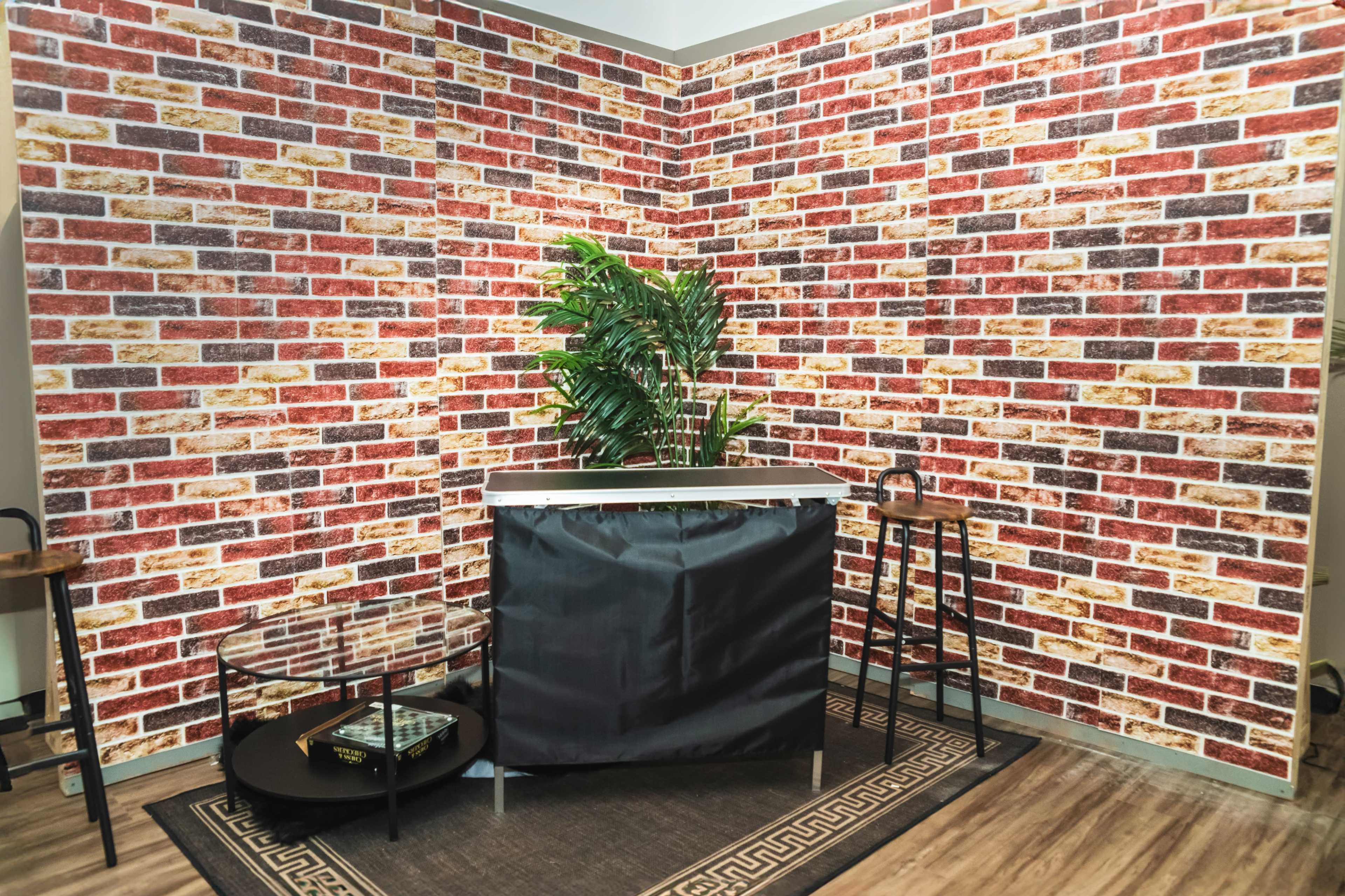 A corner workspace featuring a faux brick wall, a black divider, a glass coffee table, and two bar stools.