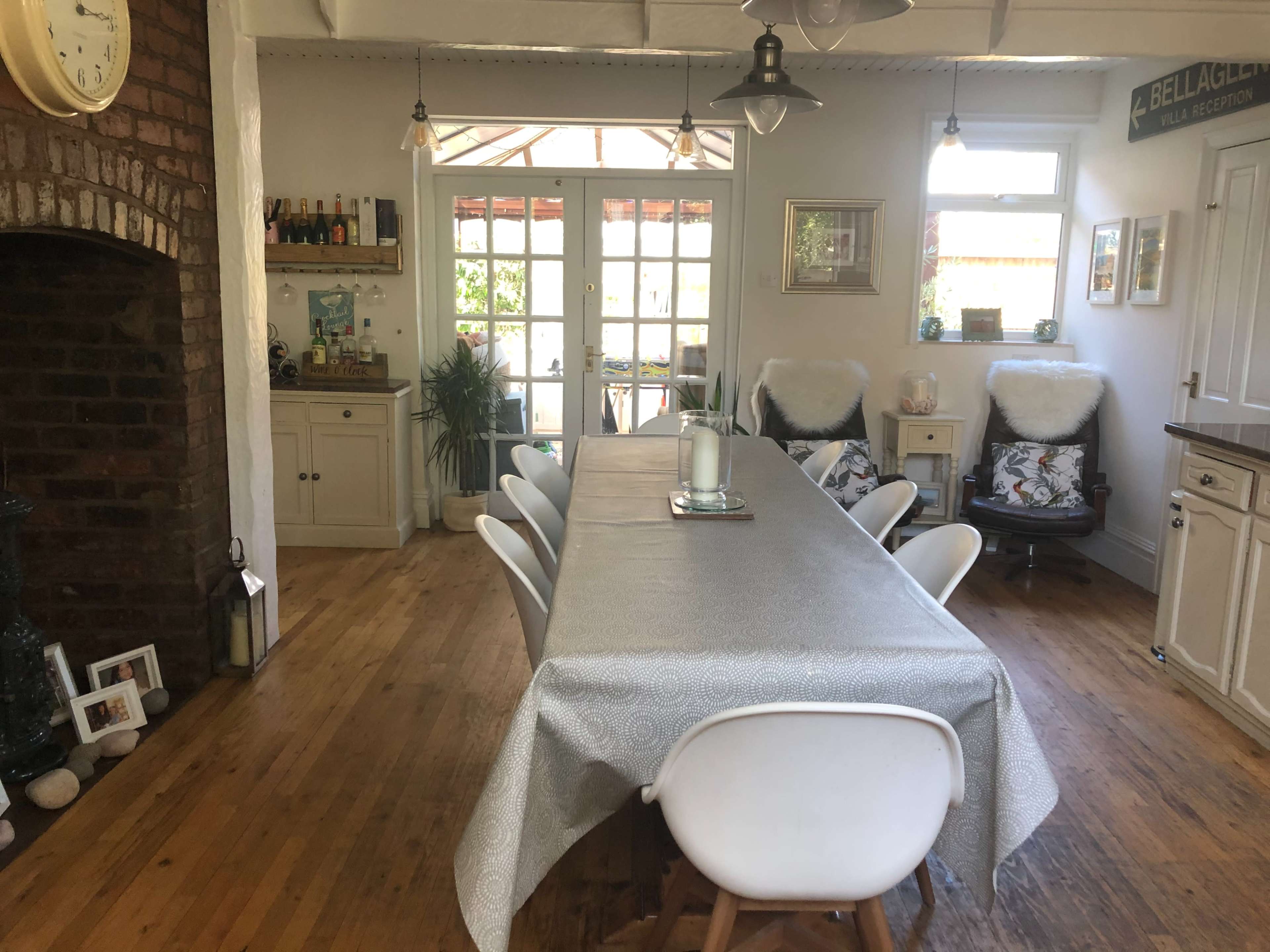 The dining area features a long table surrounded by white chairs, with a brick fireplace and large glass doors leading to a patio.