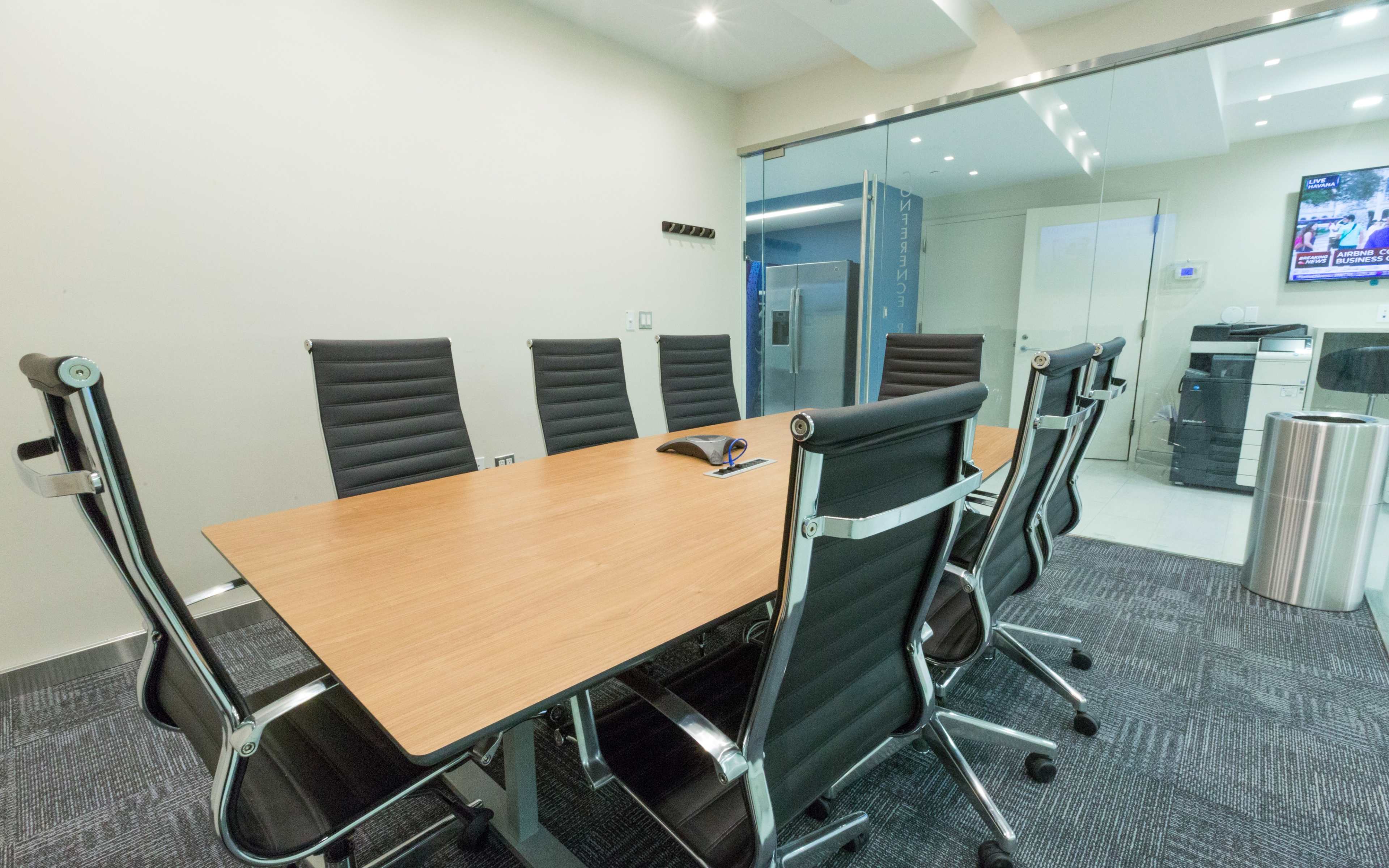 A modern conference room features a wooden table surrounded by black ergonomic chairs and a glass wall.