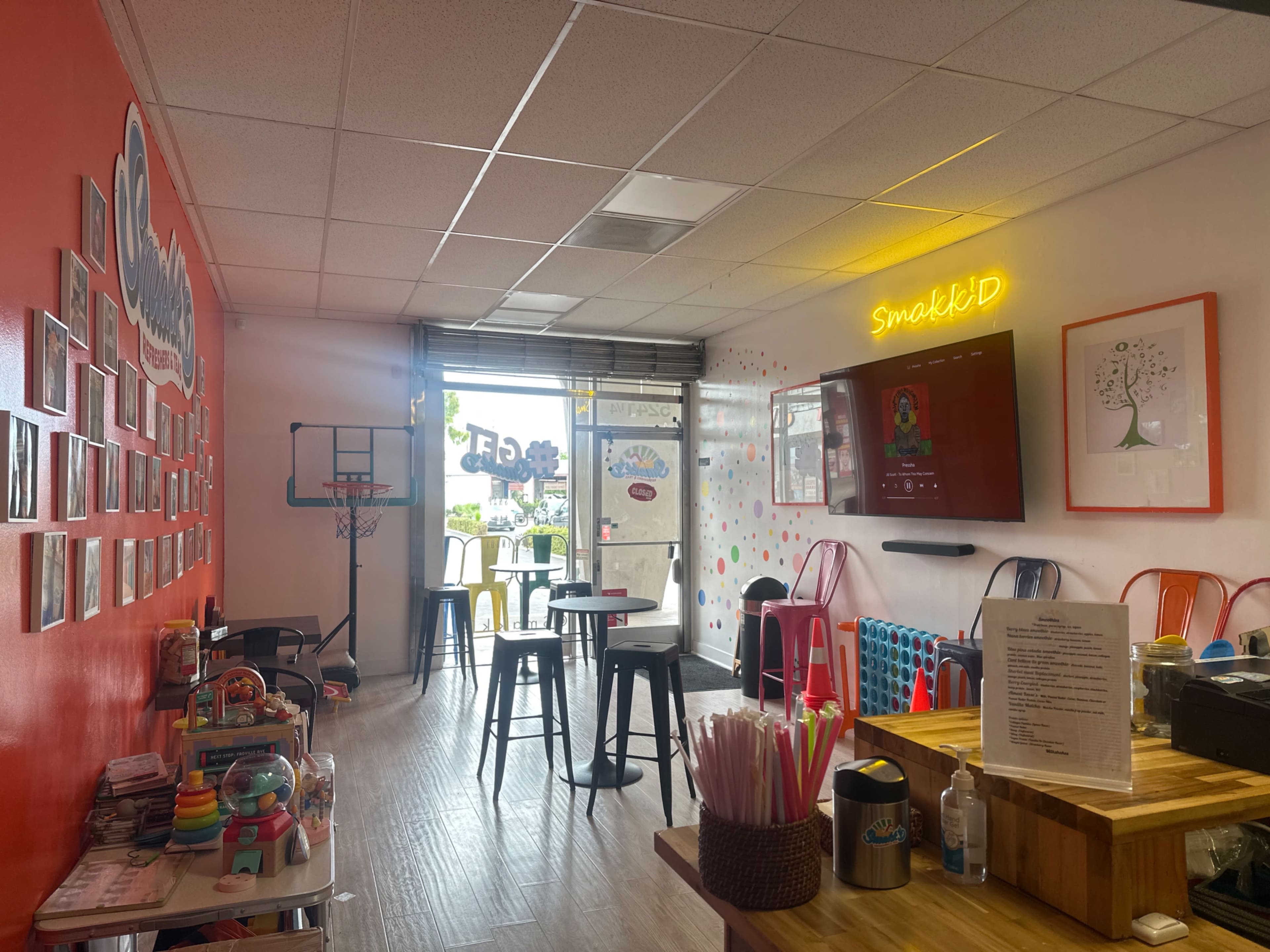 The image shows a brightly colored café interior with stools, a basketball hoop, and shelves displaying various toys and games.