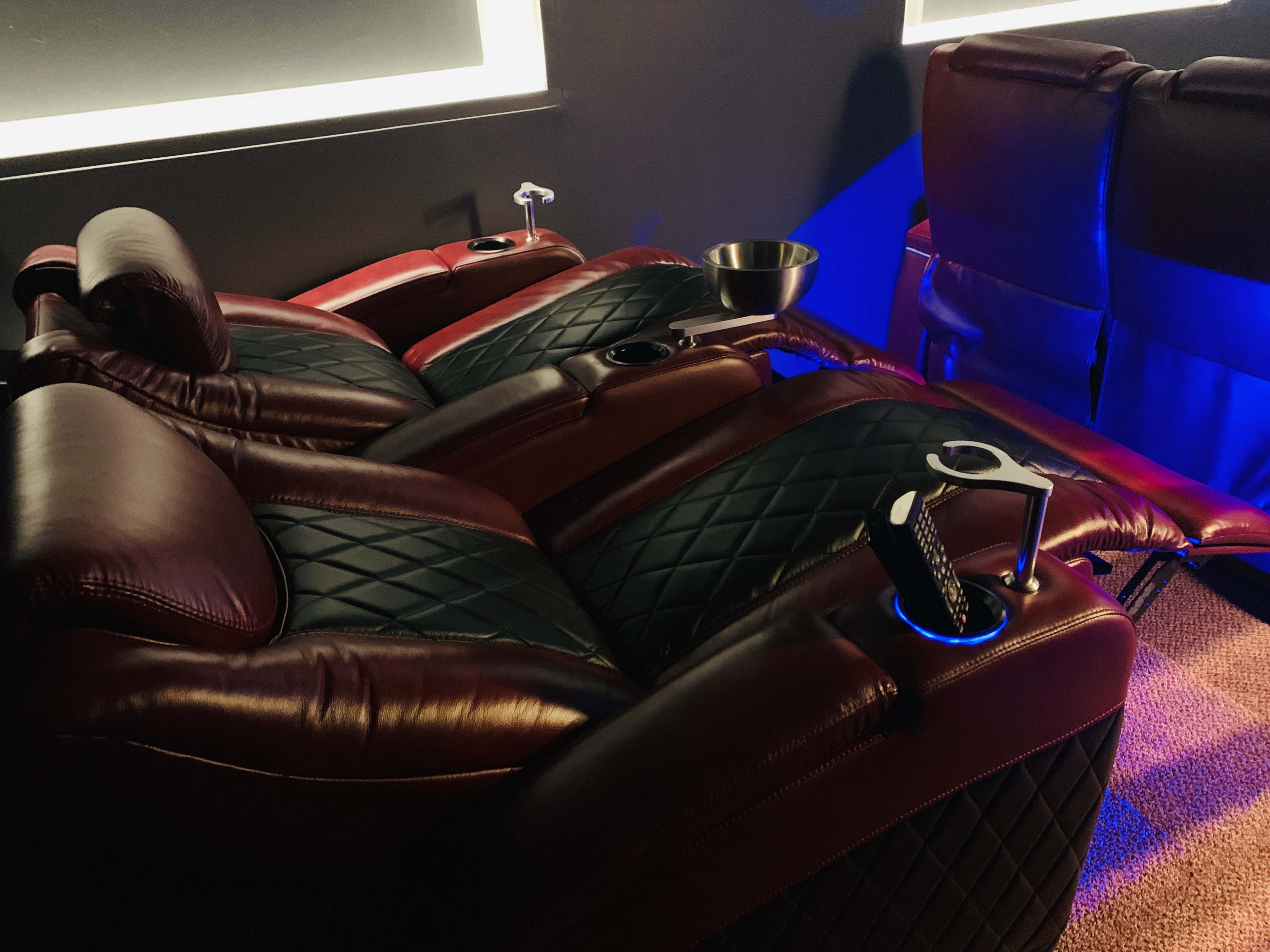 Plush reclining chairs with quilted leather upholstery and built-in cup holders in a dimly lit room.