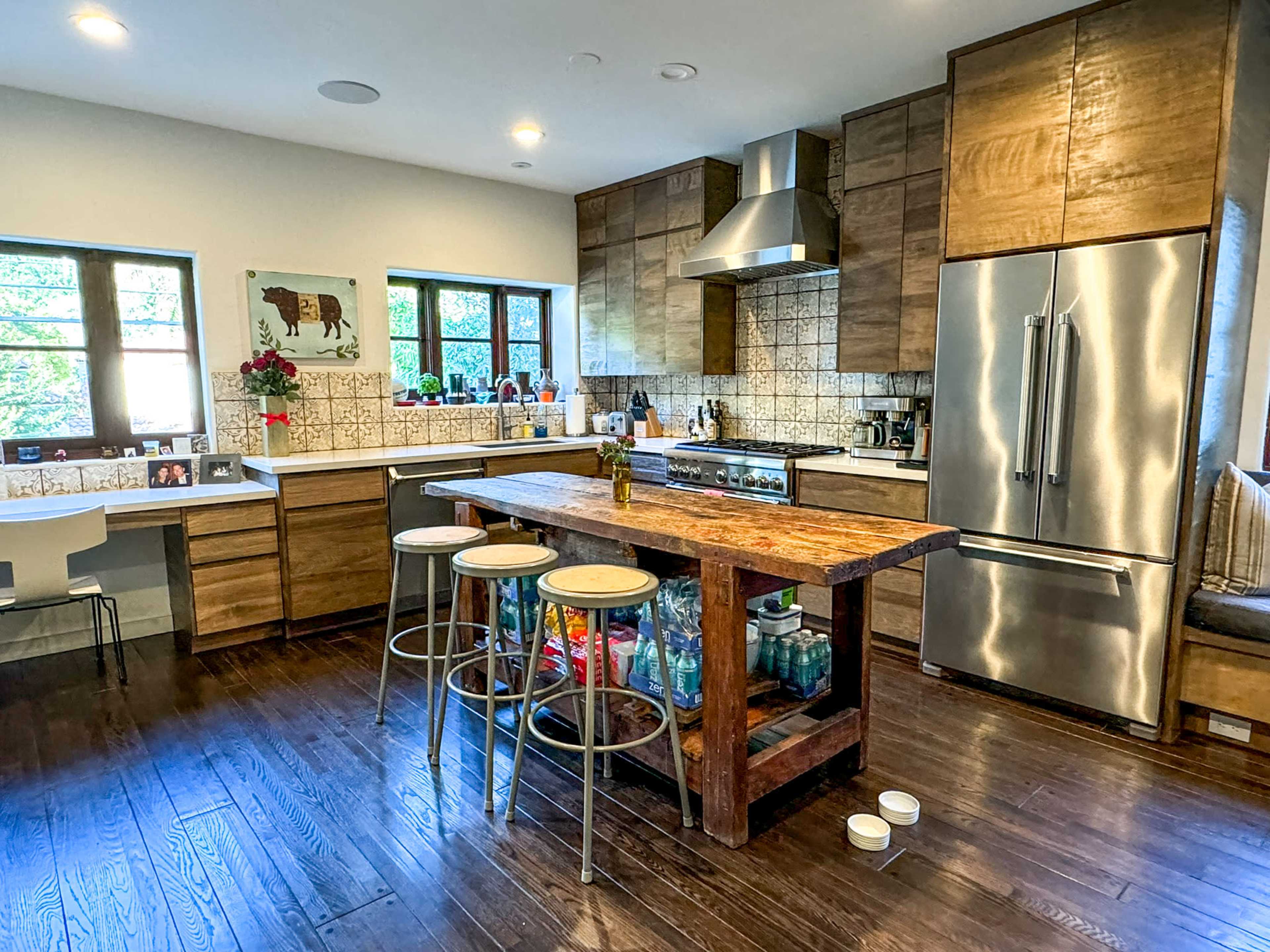 A modern kitchen features a large wooden island with bar stools, sleek stainless steel appliances, and a mix of light and dark wood cabinetry.