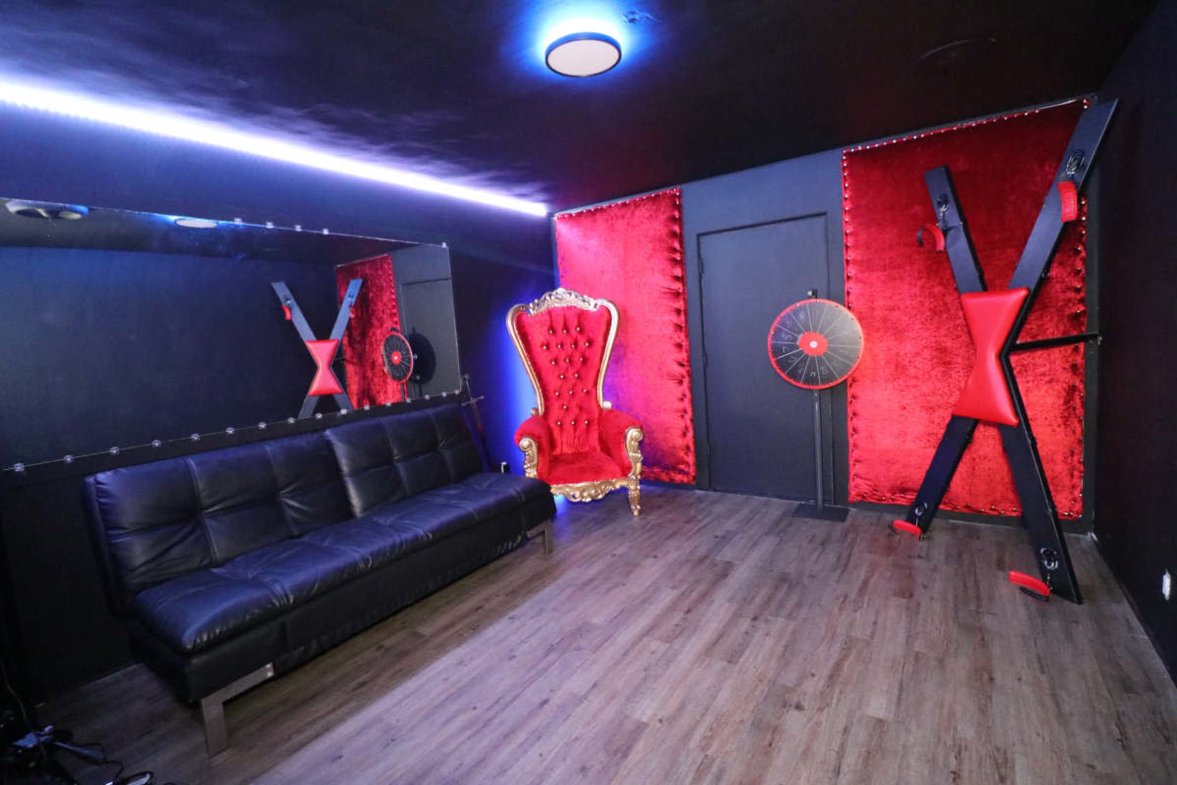The room features a black sofa, a red velvet throne, and a mirrored wall with dramatic lighting.