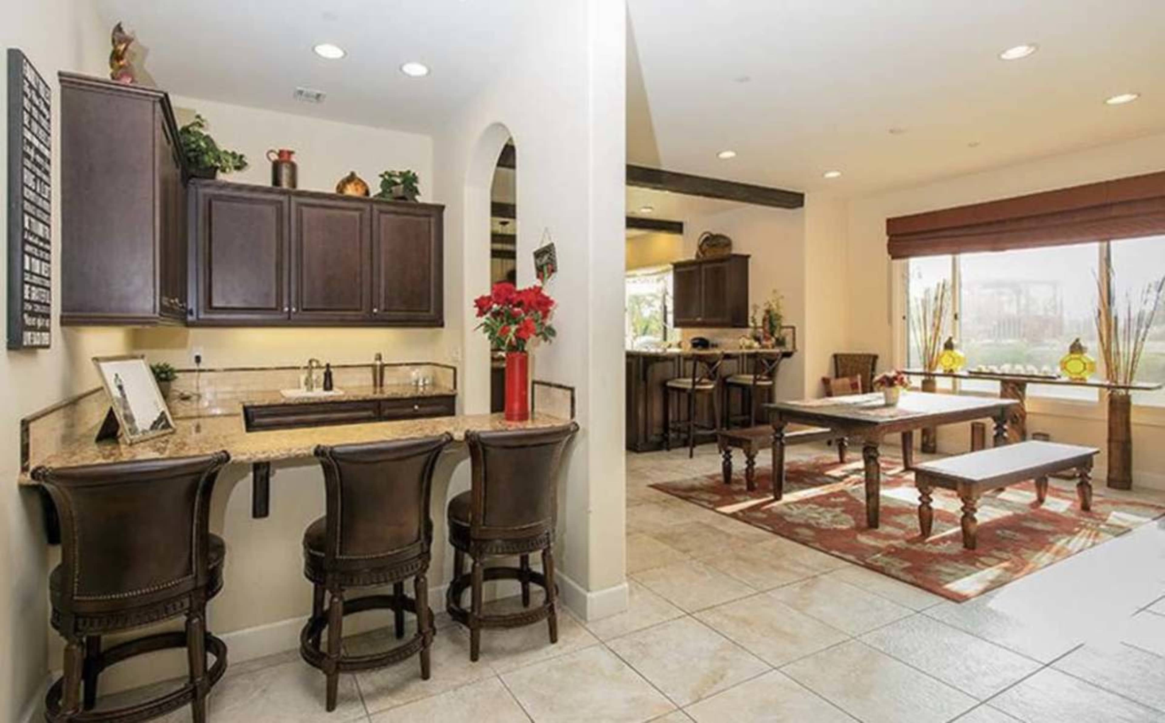 The image shows a modern kitchen area with a granite countertop and bar seating, leading into a dining space with a wooden table and benches.